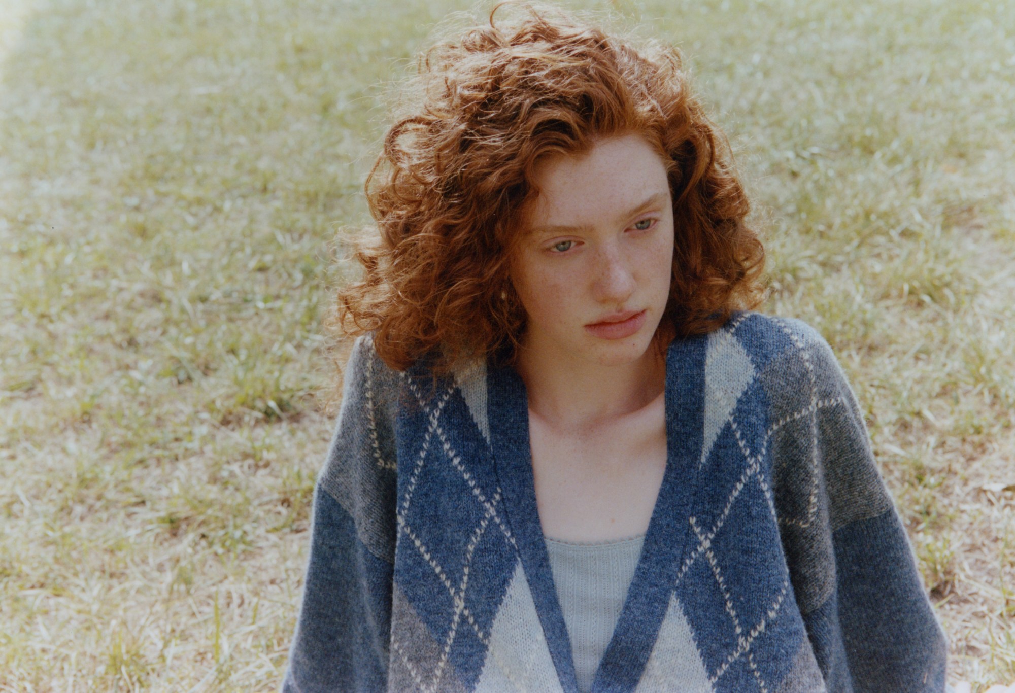 A teenager with red hair sat in a field staring into the distance