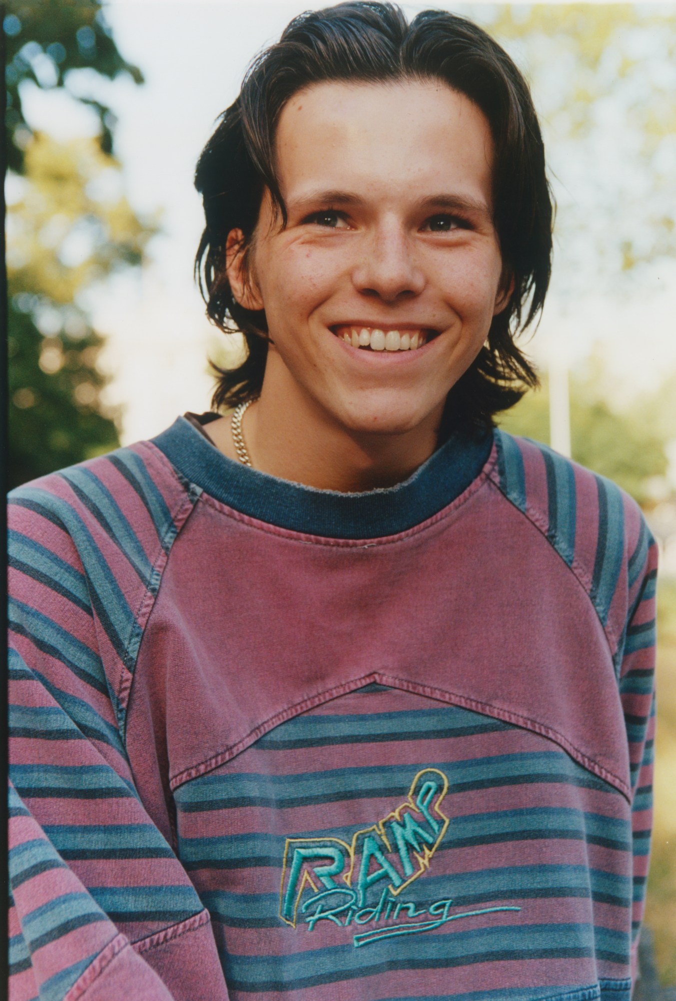 A teenager in a blue and pink striped t-shirt grinning