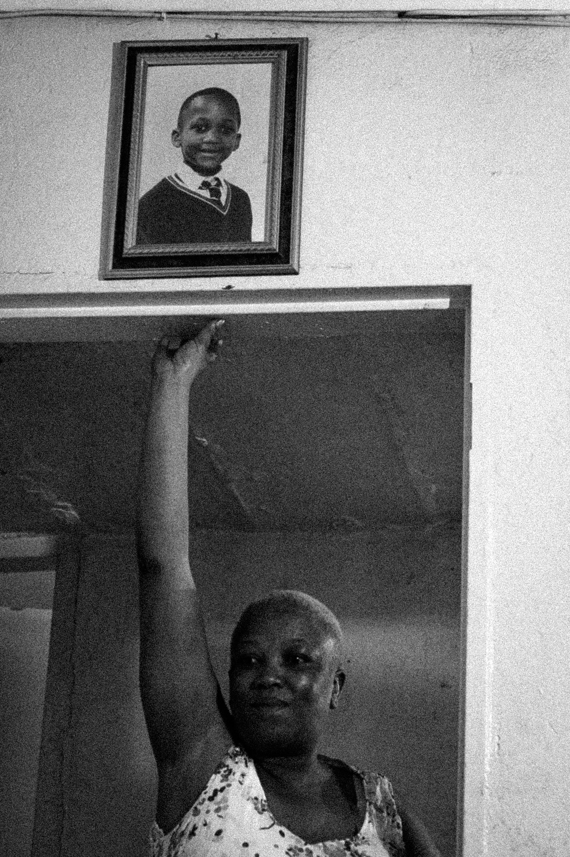 black-and-white image of a woman reaching up to touch a door frame where a picture of a child hangs on the wall