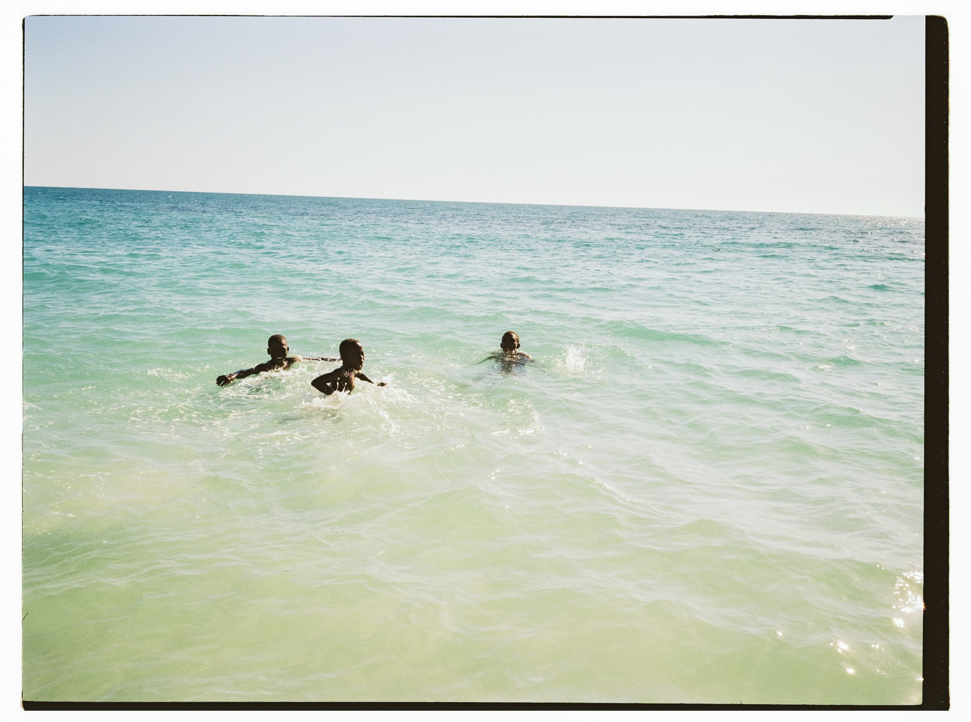 three people swimming in sunny blue-green waters