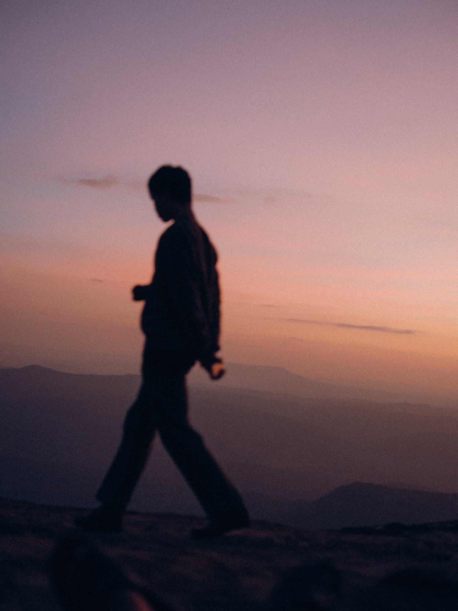 blurry image of a man walking across a mountain range at sunset