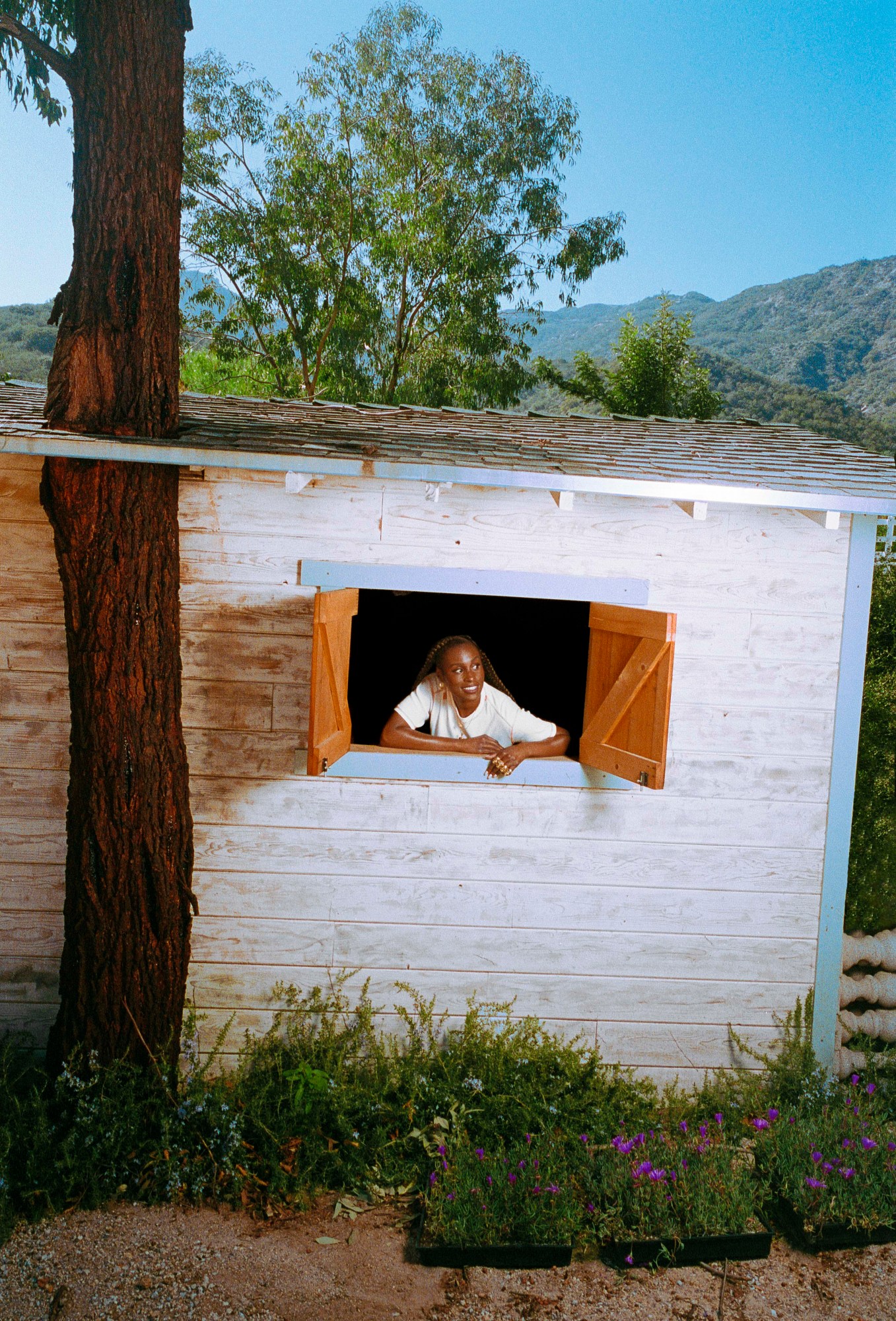 issa rae peeping out the window of a white washed wooden beach hut