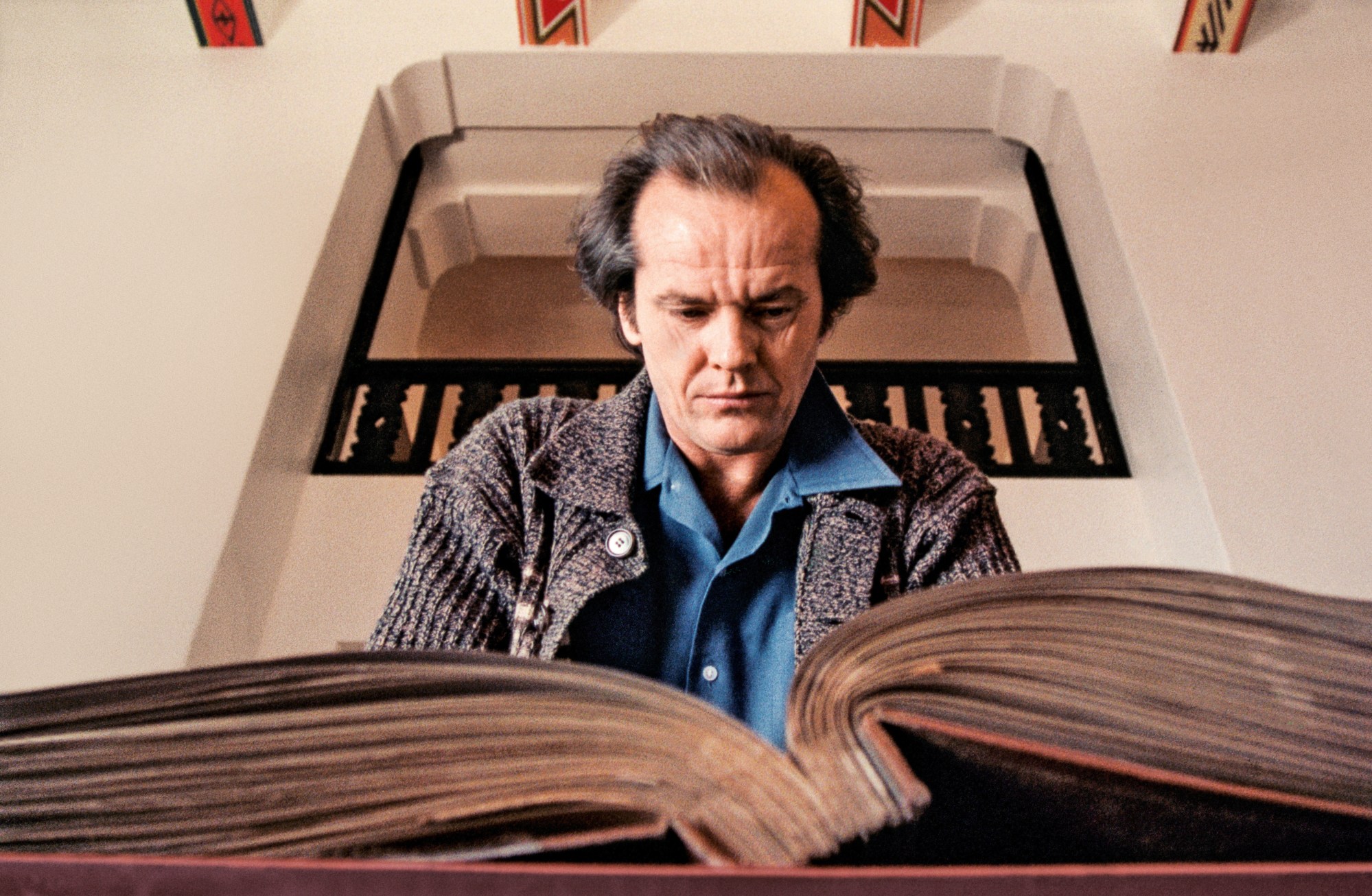 a still of jack nicholson in the shining, looking through a photo book.