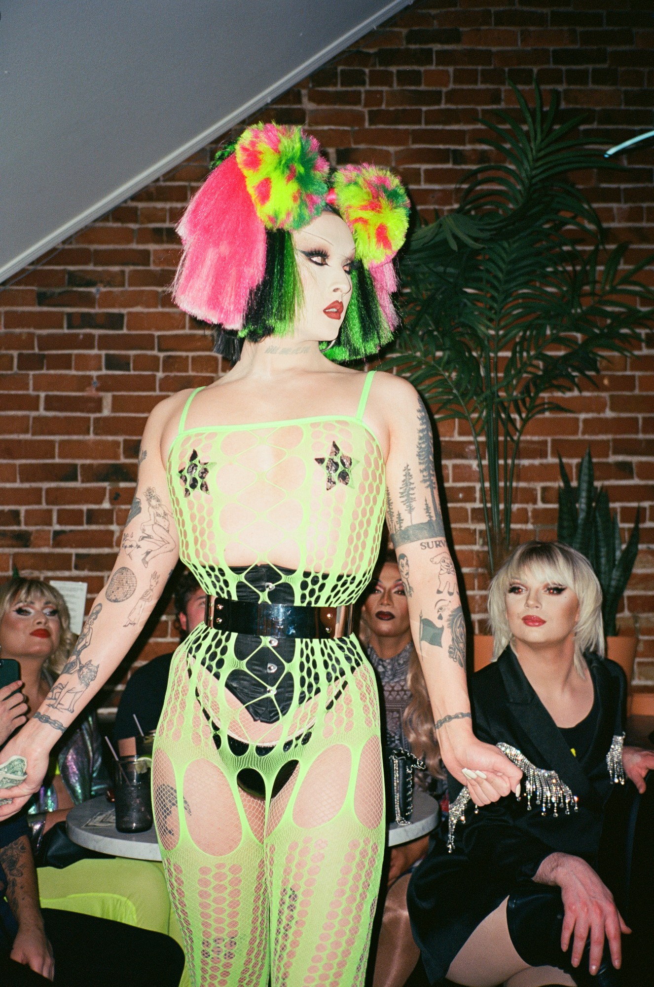 a drag queen performing in a bar wearing a neon green cut out gown