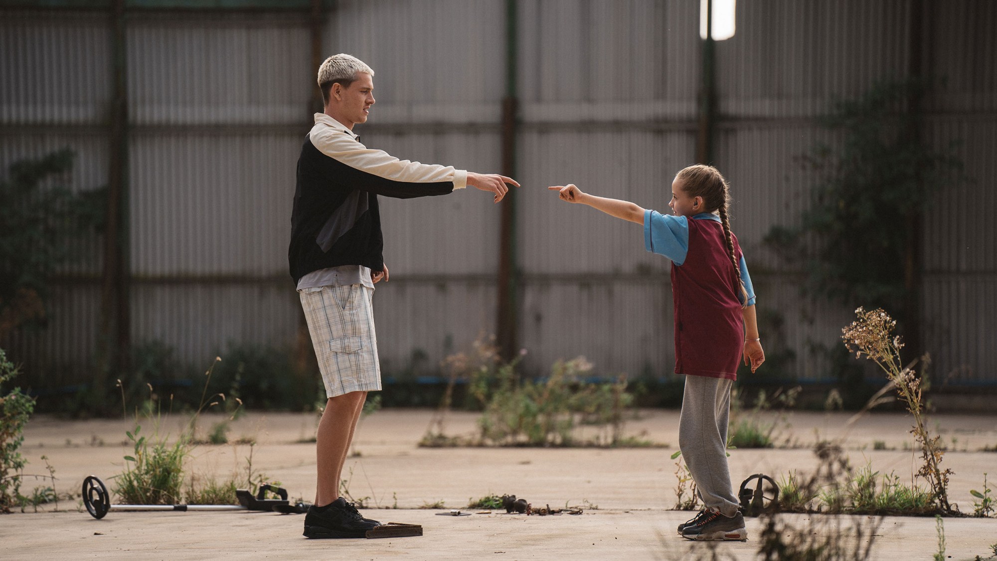 a young man with bleached hair reaches out to a little girl whose arm is also outstretched, the pair almost touching fingers