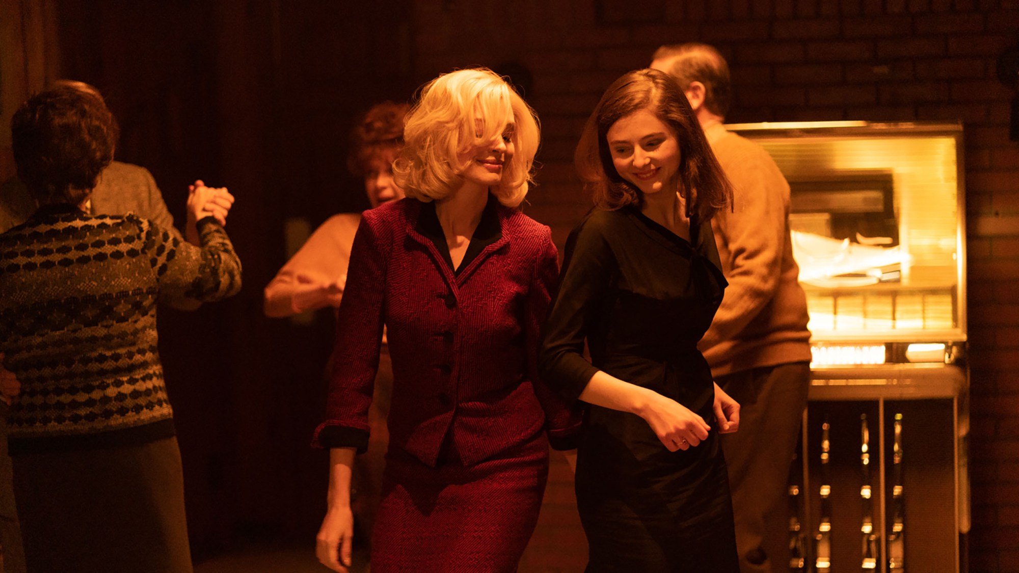 two young women, one blonde and one brunette, dance together among older dancers