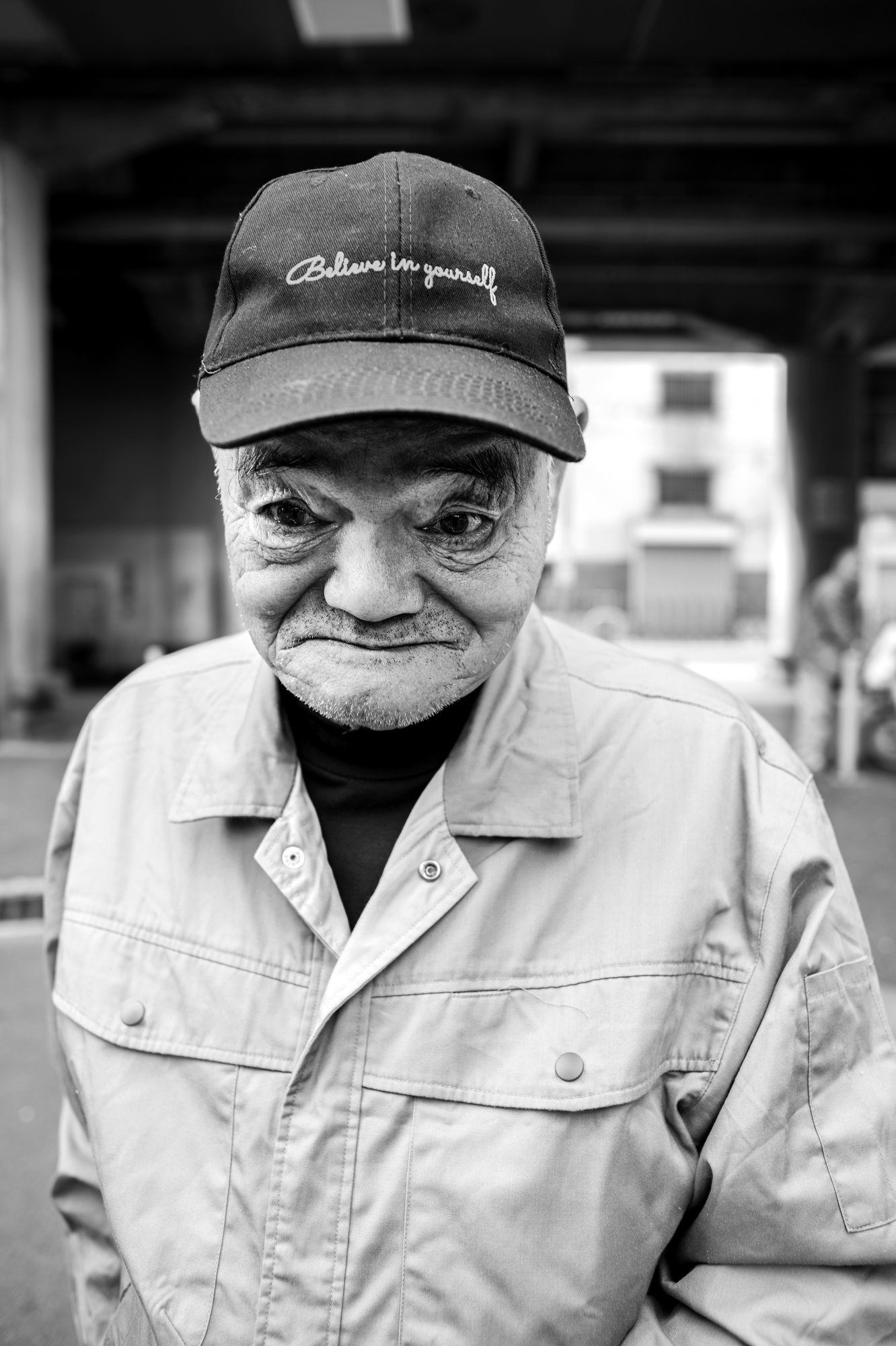 black-and-white image of a male day labourer wearing a baseball cap that says believe in yourself