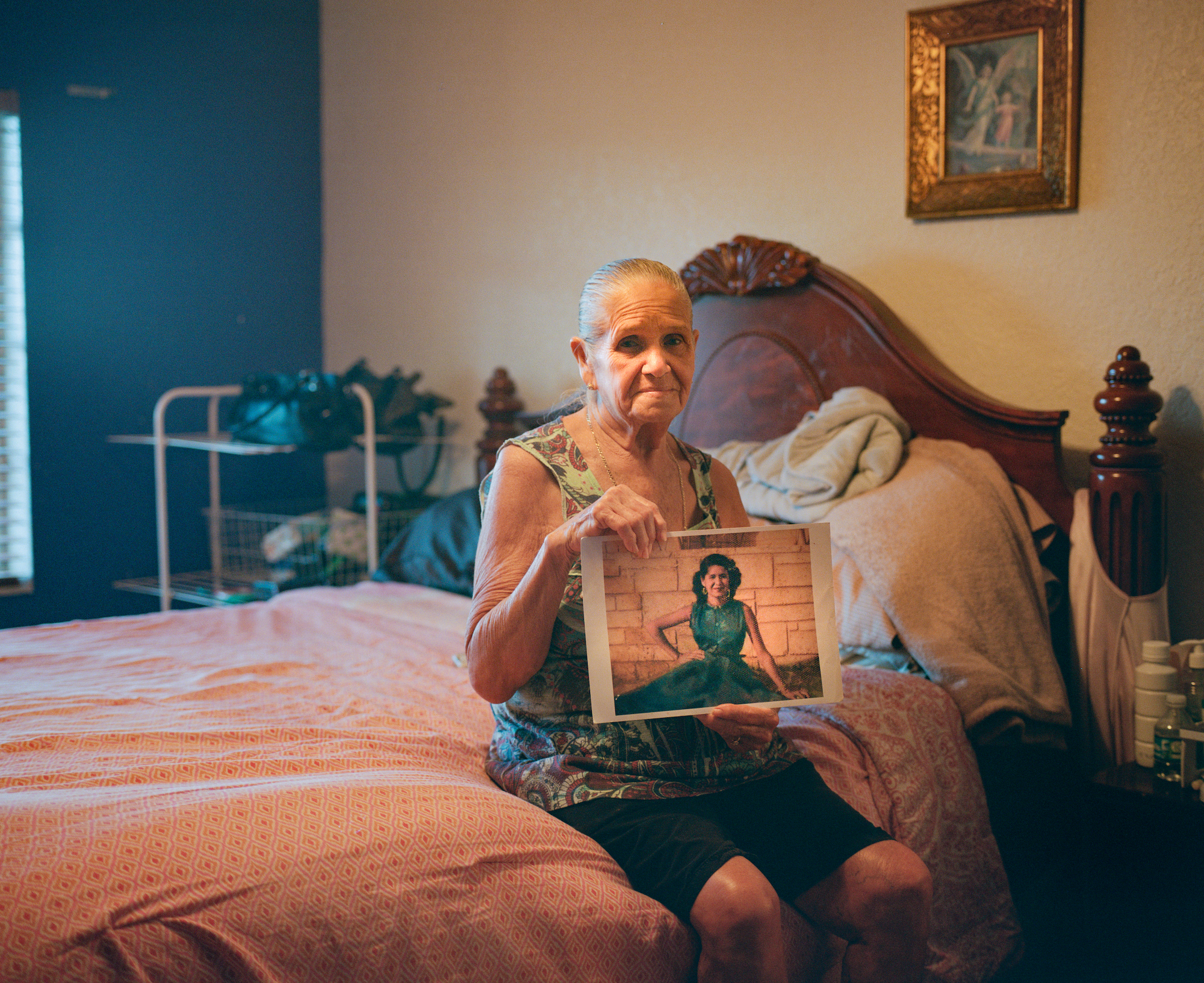 an old woman sitting on a bed holding an old photo of herself