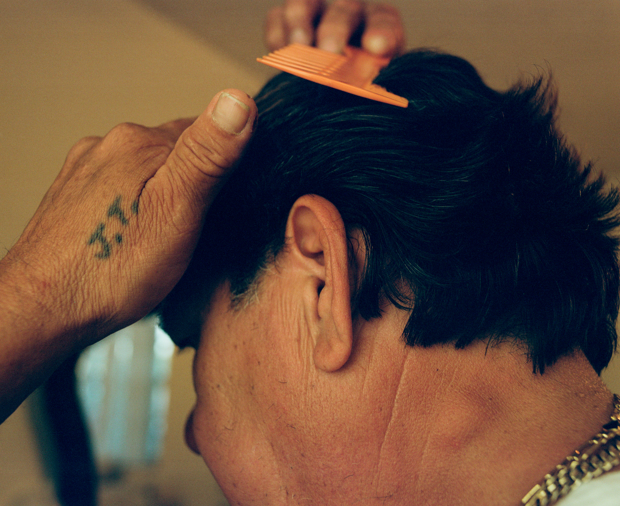 close-up image of a man brushing his hair with an orange comb, a tattoo on his hand reads J.T