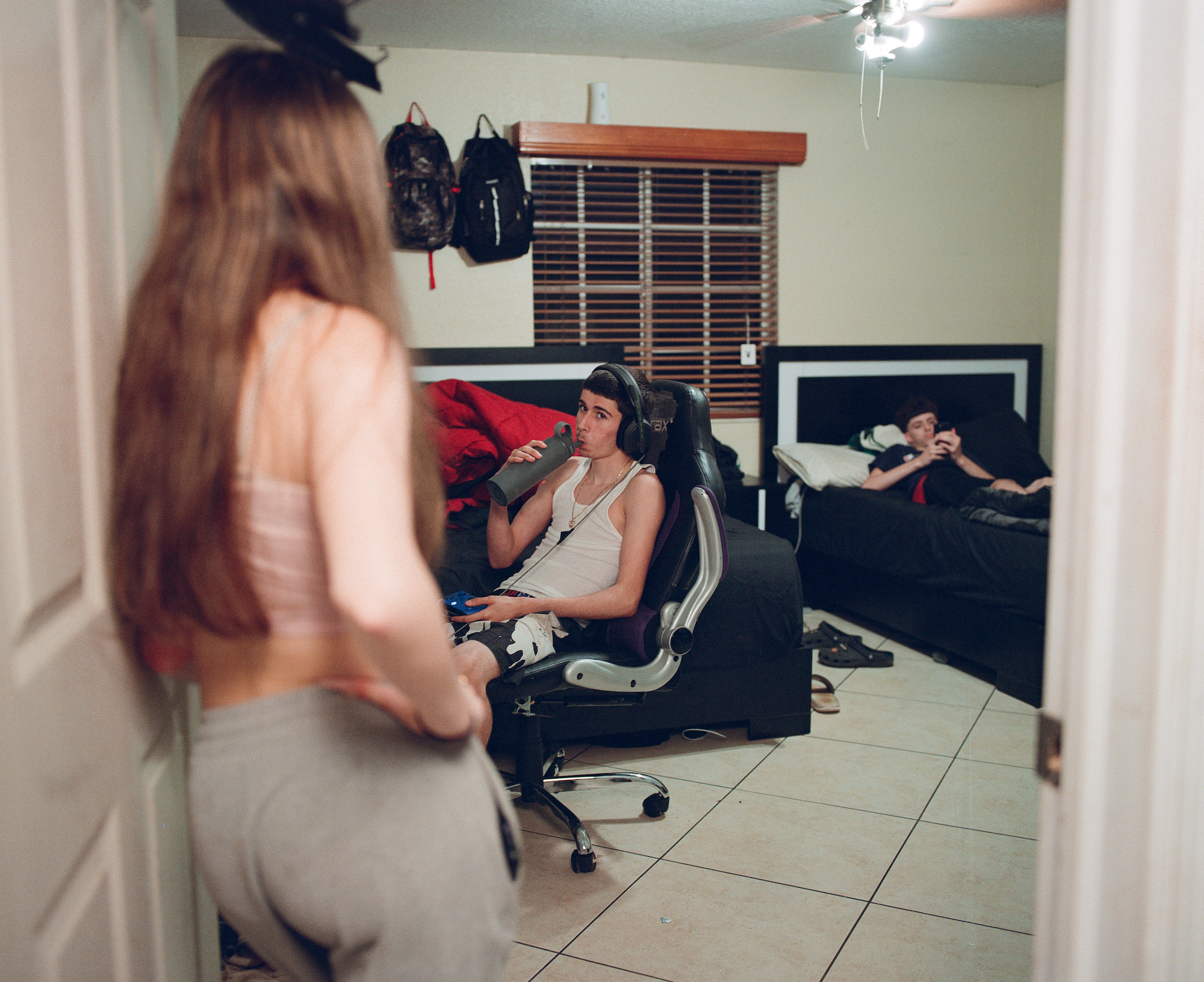 a girl standing in a doorway with her hand on her hip and two boys lounging in chairs