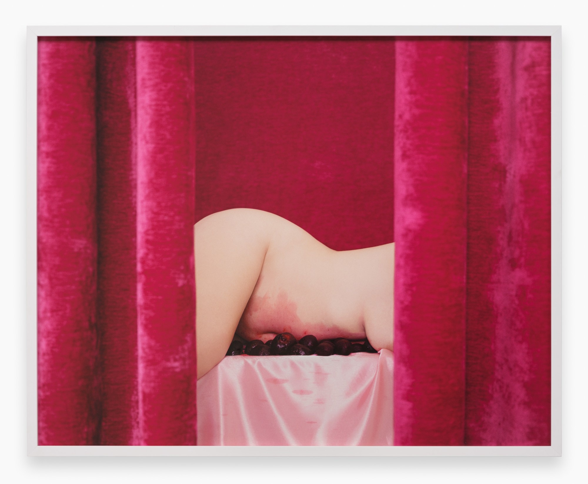 a naked woman lying on a pink bed of plums behind pink velvet curtains