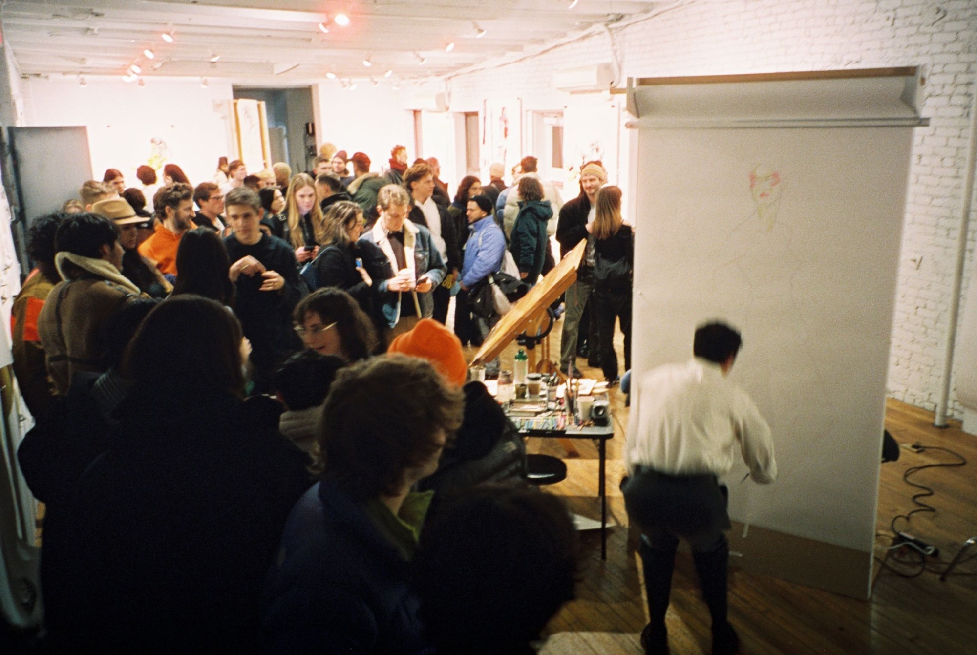 the artist drake carr draws on a white canvas while a crowd gathers in his studio