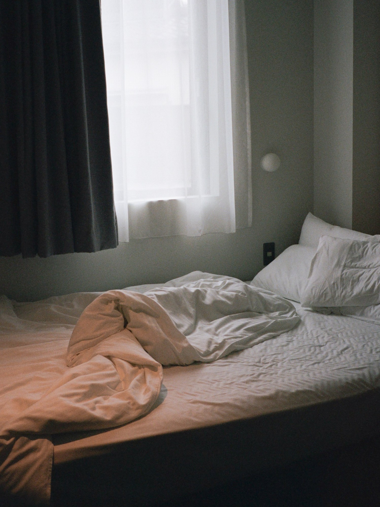 an unmade bed with white sheets next to a window