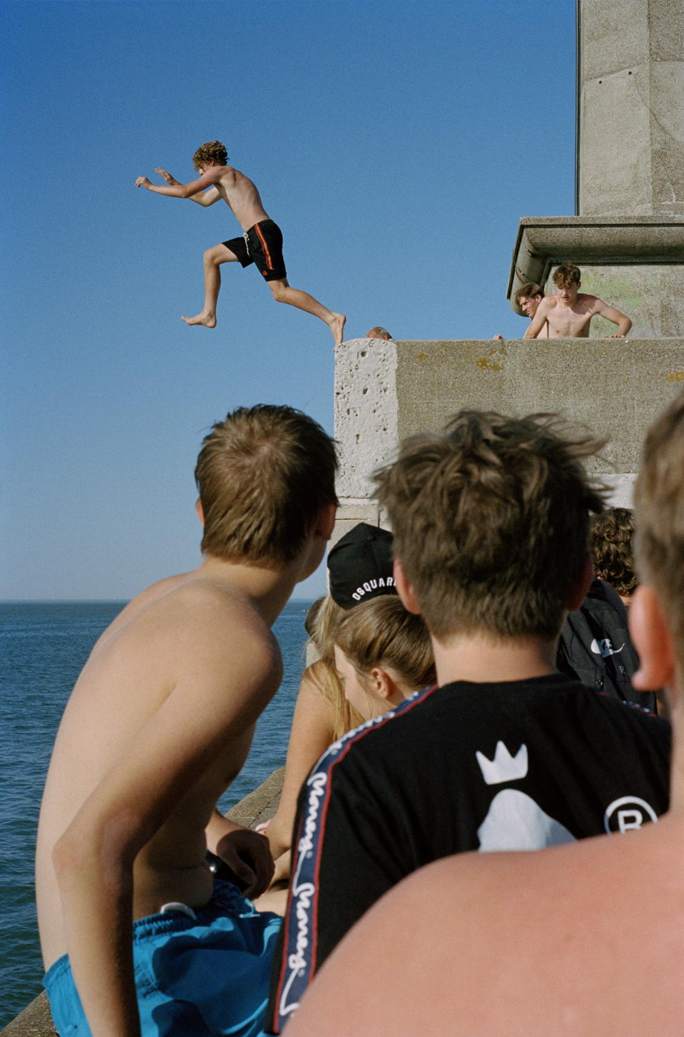 a boy jumping into the water and people looking on