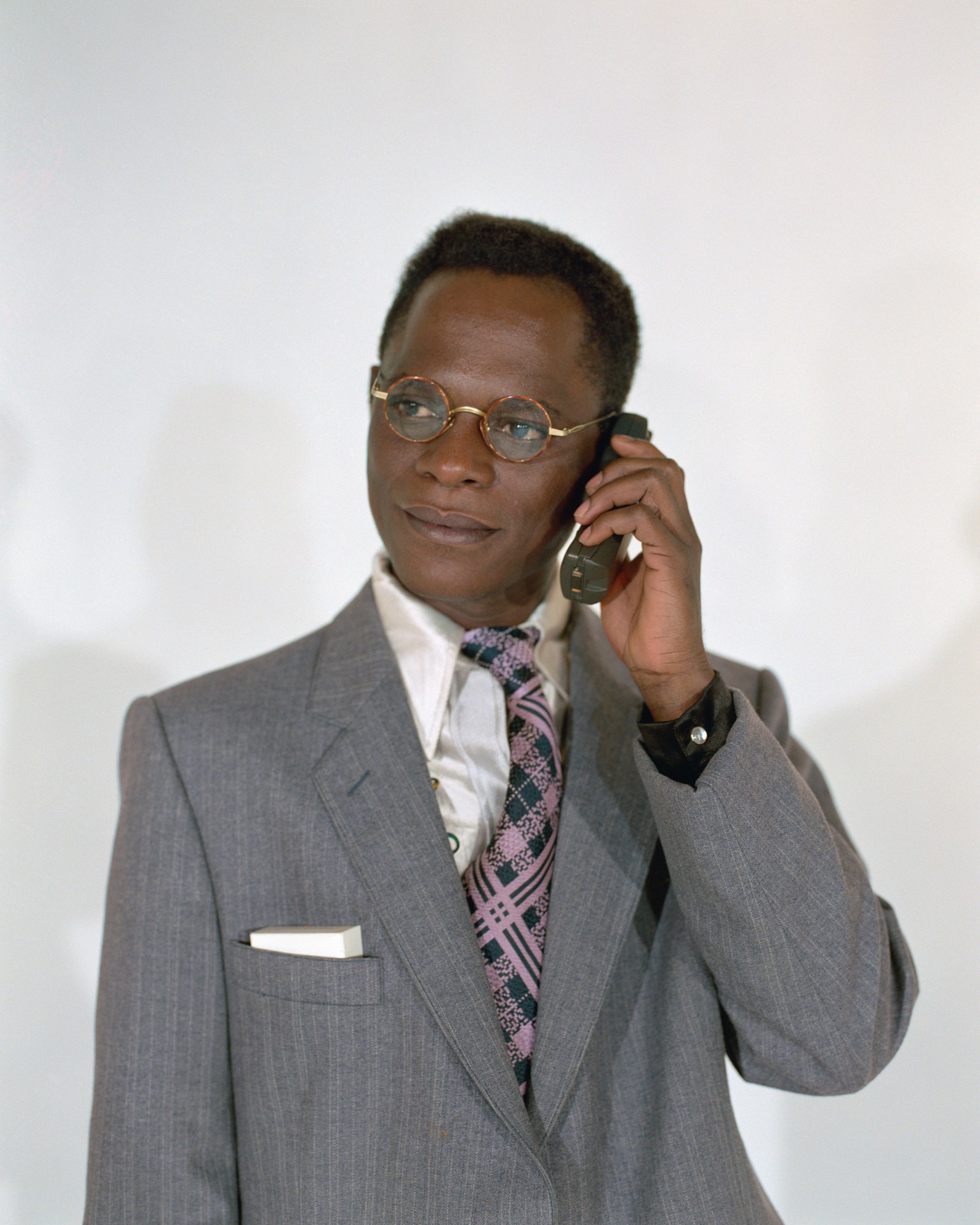 Samuel Fosso wearing a grey suit and eyeglasses in his studio.