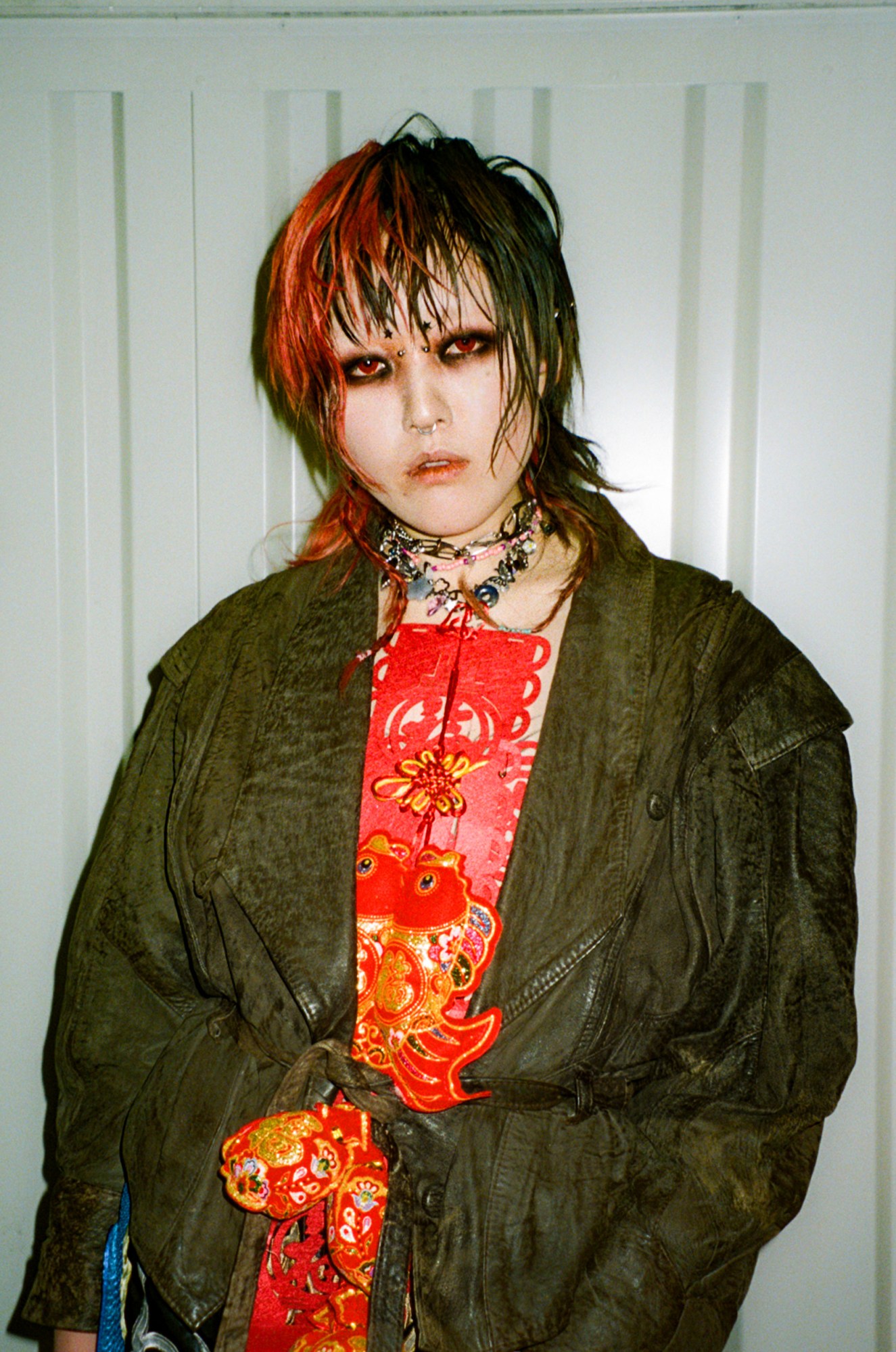 a young person poses wearing a leather jacket over a top constructed of lunar new year decorations