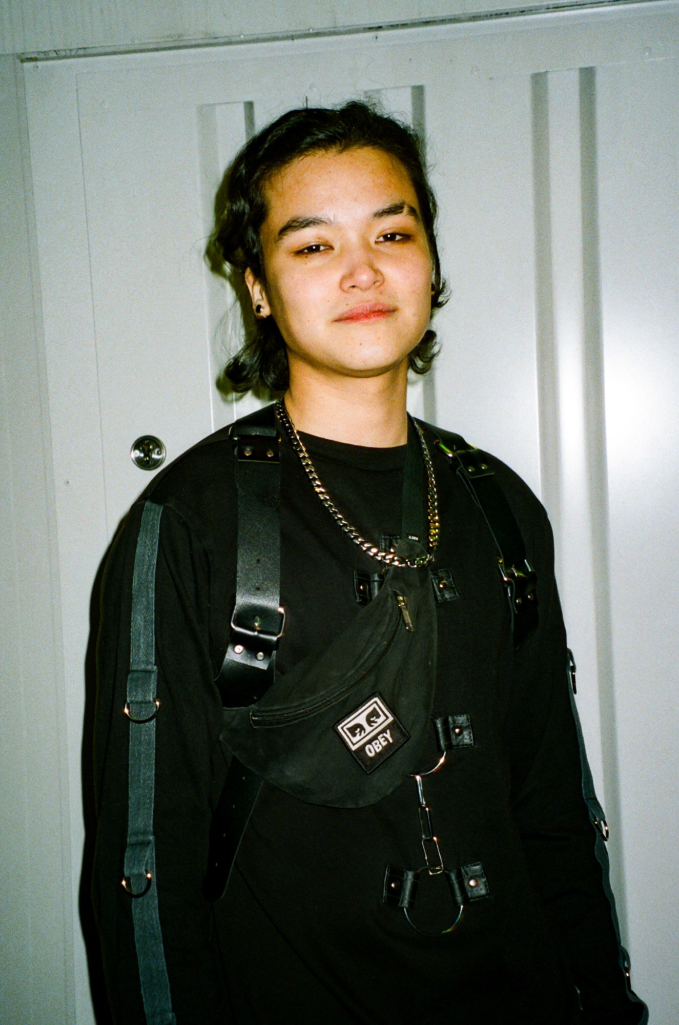 robin wears all black, with a leather harness and a cross-body obey bag with a gold chain