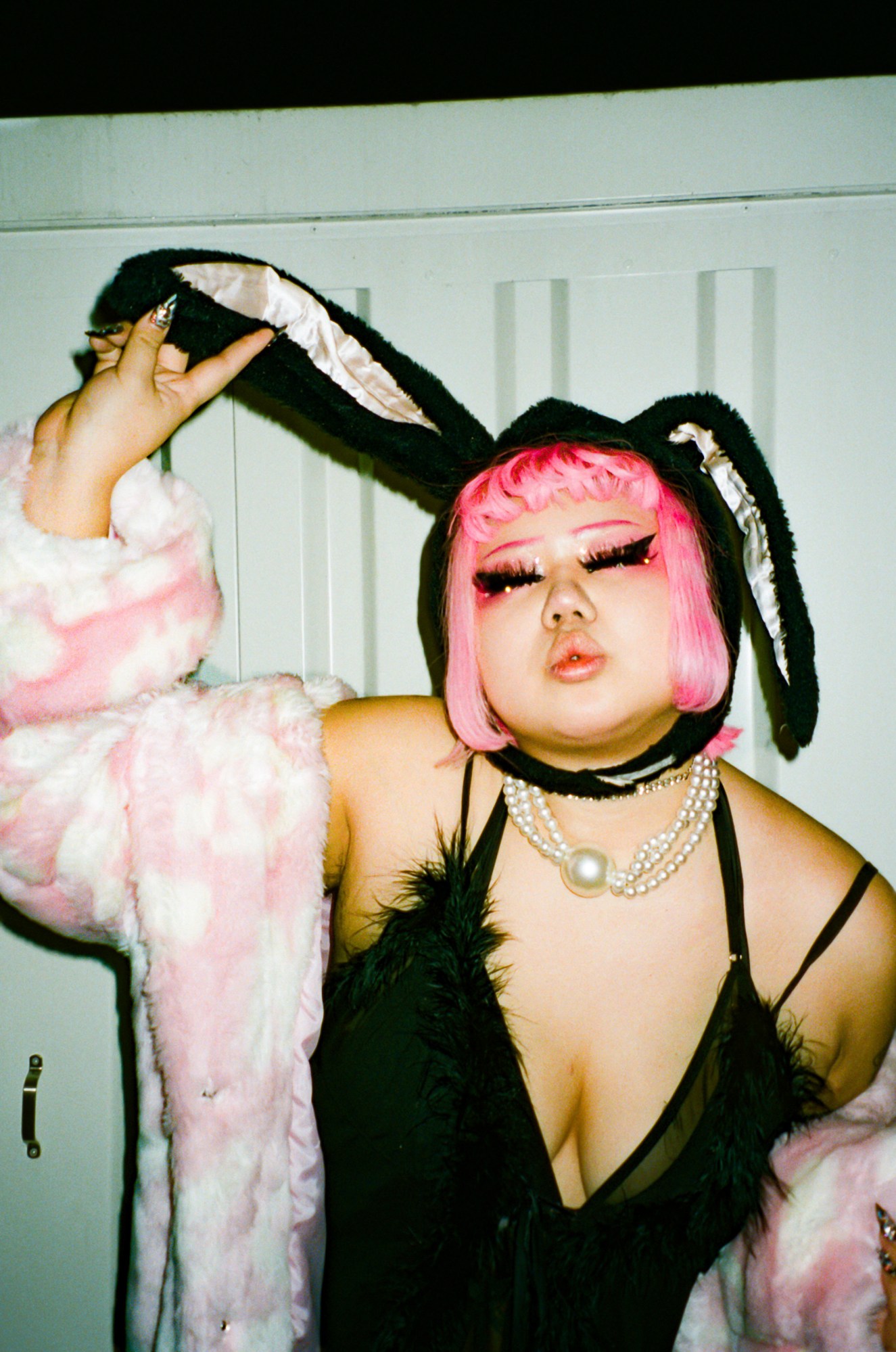 a person poses wearing a slip dress, a fluffy pink coat, a pink wig and bunny ears