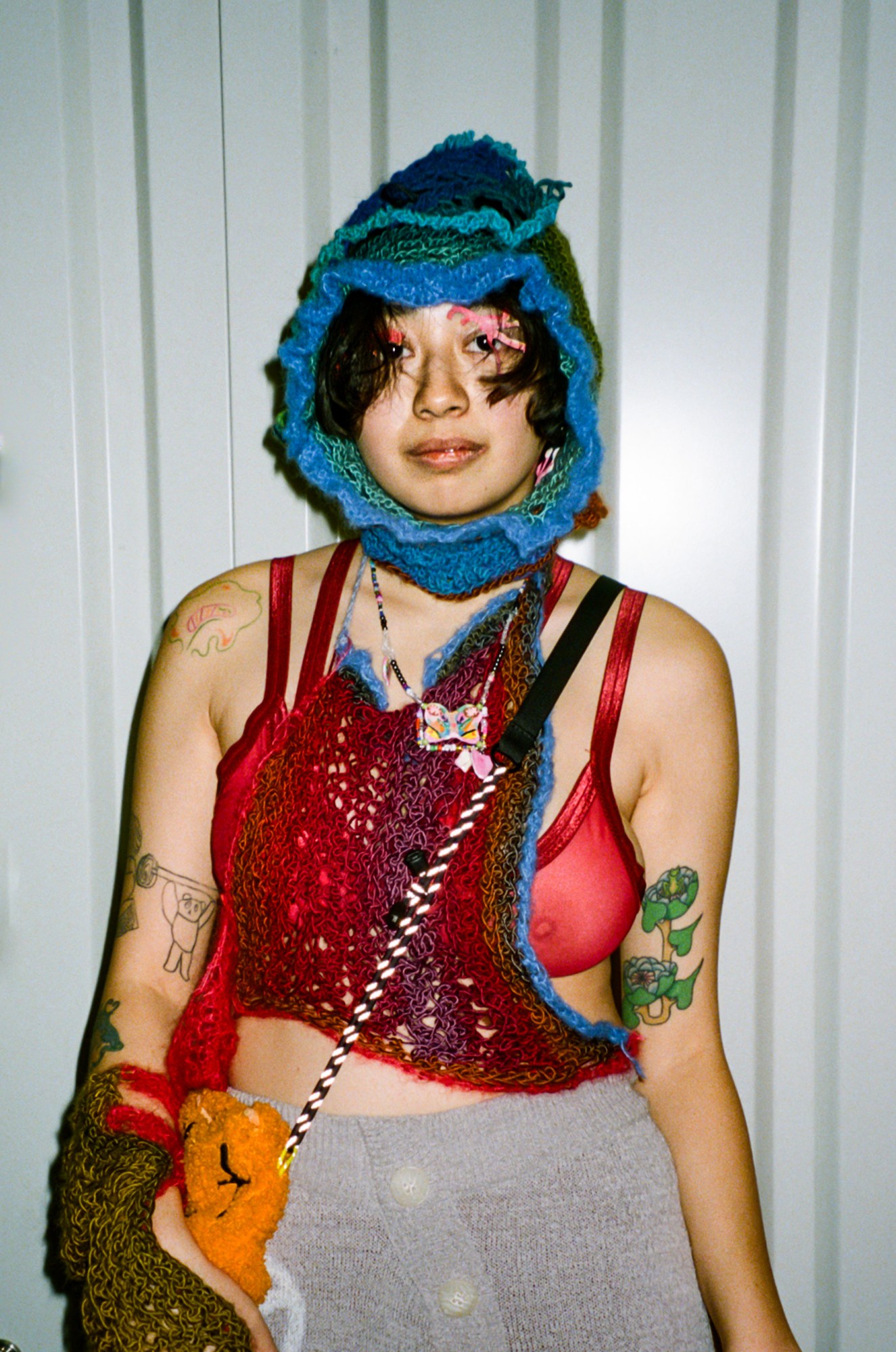 a person with colourful tattoos wears several crochet pieces: a halter, a balaclava, arm warmers, a skirt