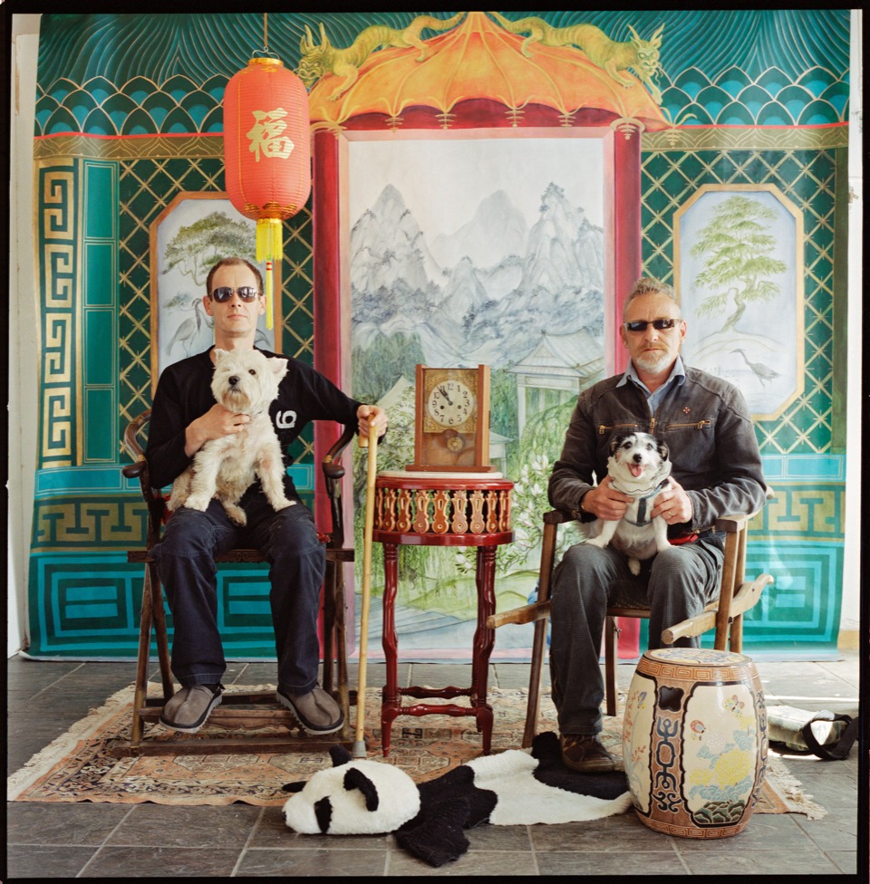 two models wearing sunglasses and holding dogs pose in the studio