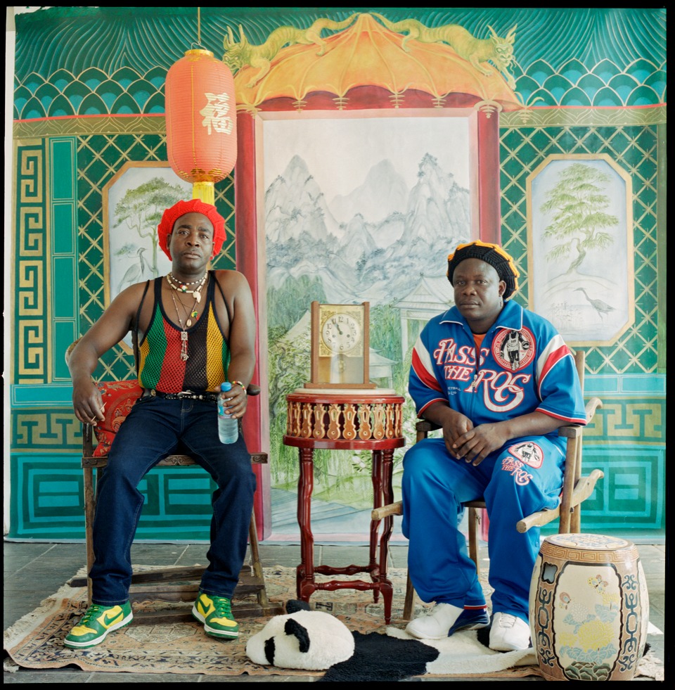 two models sit in the chinese studio, one holding a water bottle and the other just his hands