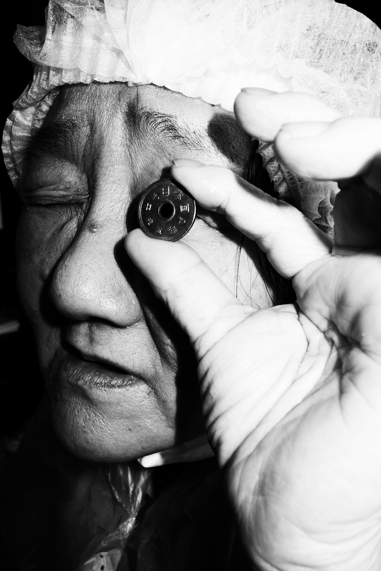 an older japanese woman peers through the hole in a 5 yen coin