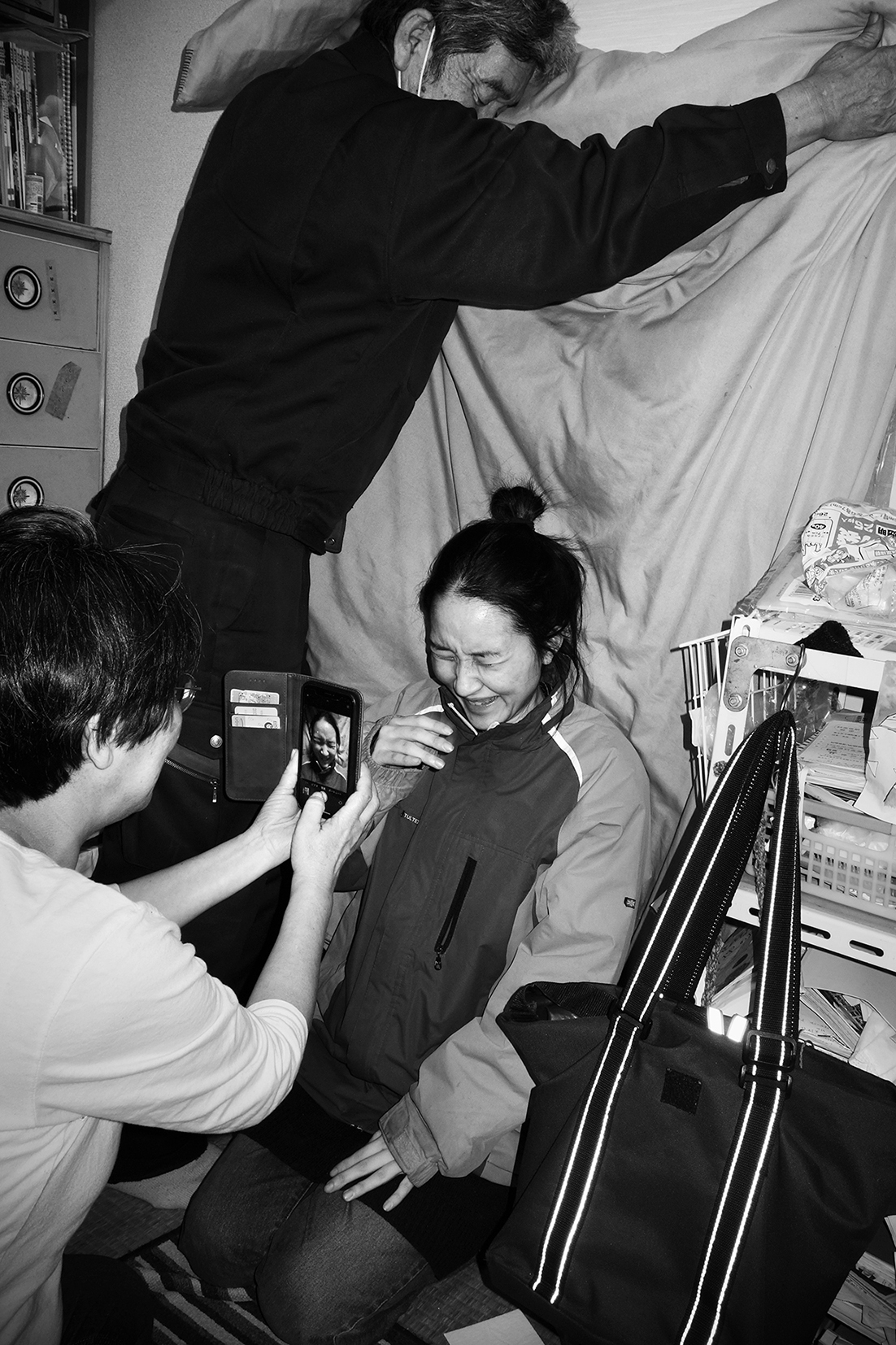 a young woman kneels in front of a sheet held up by her father; her mother takes a photograph of her smiling on her phone