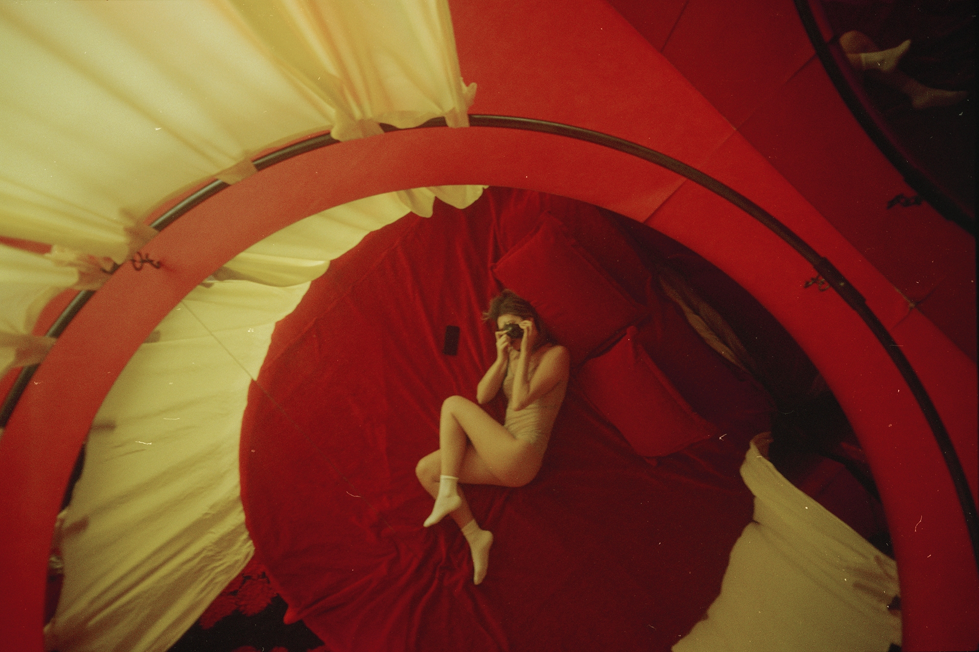 a model poses on a red circular bed, taking a photo of themselves in the mirrored ceiling