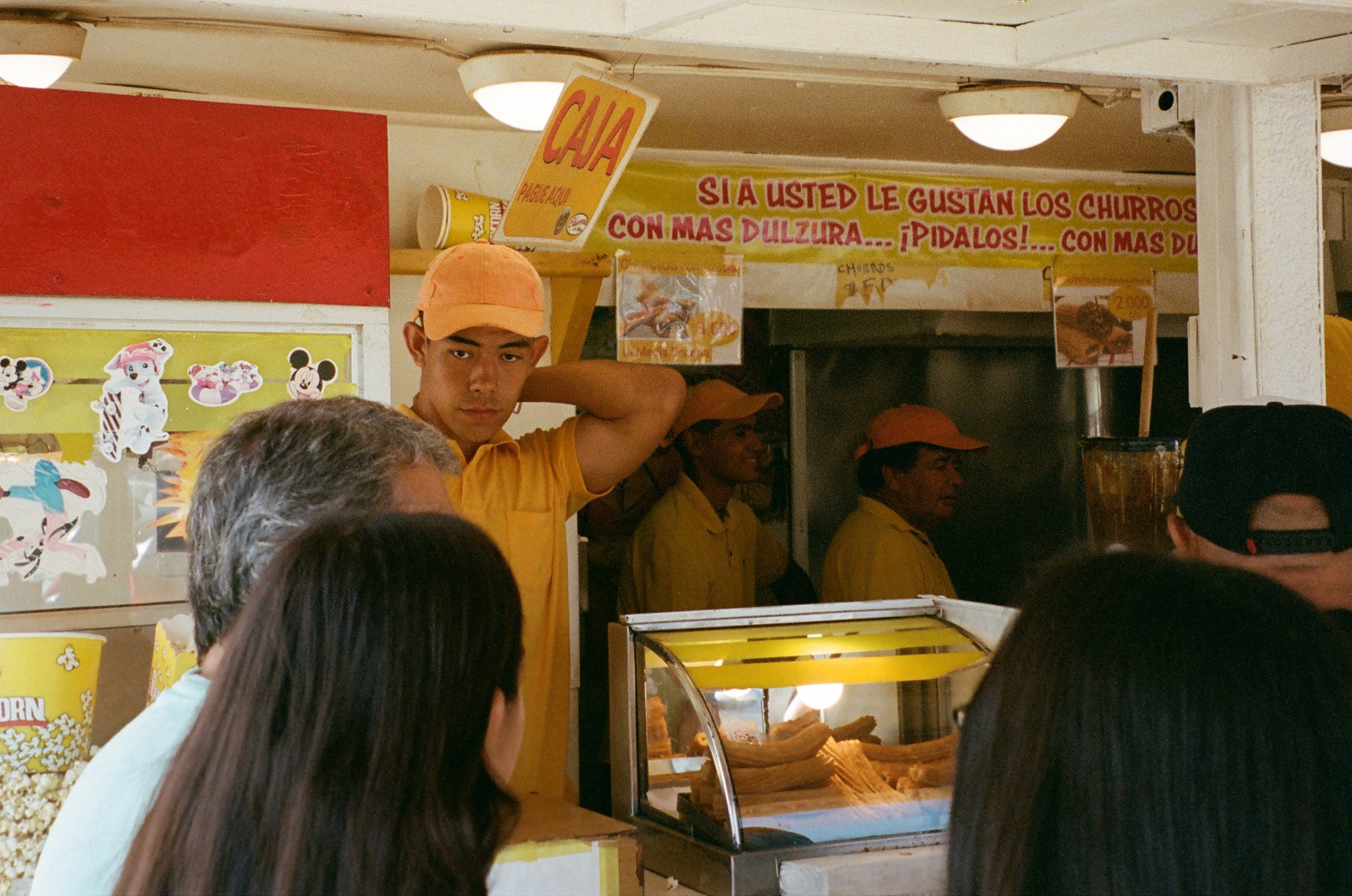 people standing in a line at a churro stand; the workers wear yellow uniforms