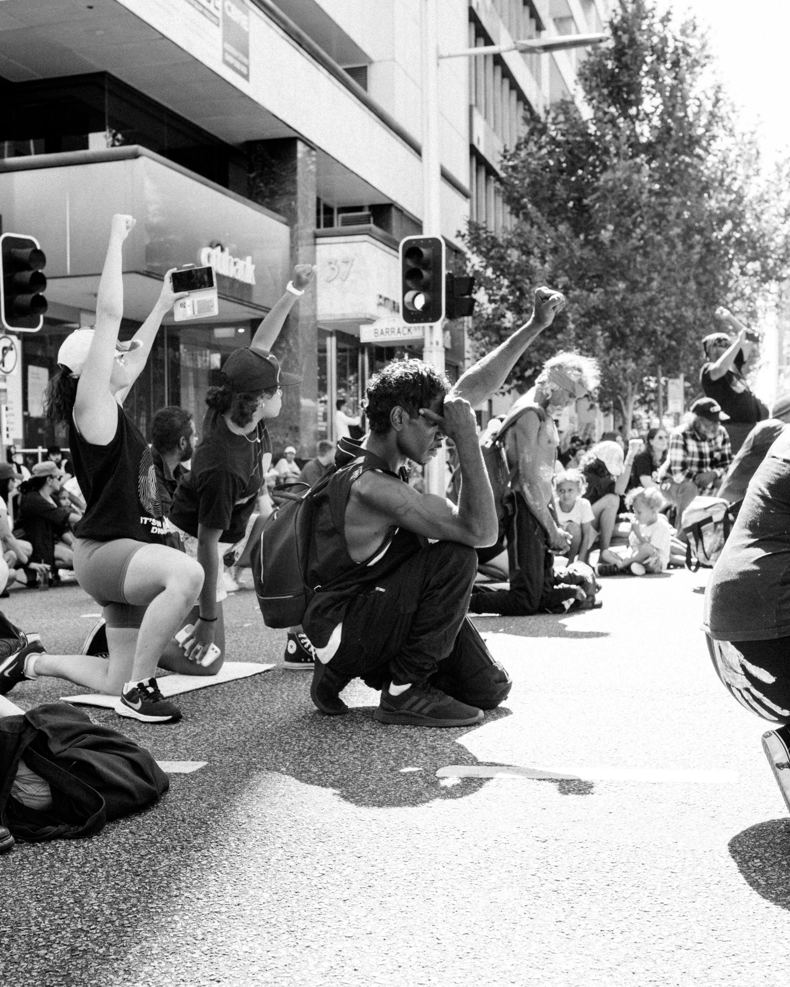 a gathering of people kneel down in solidarity, raising their fists