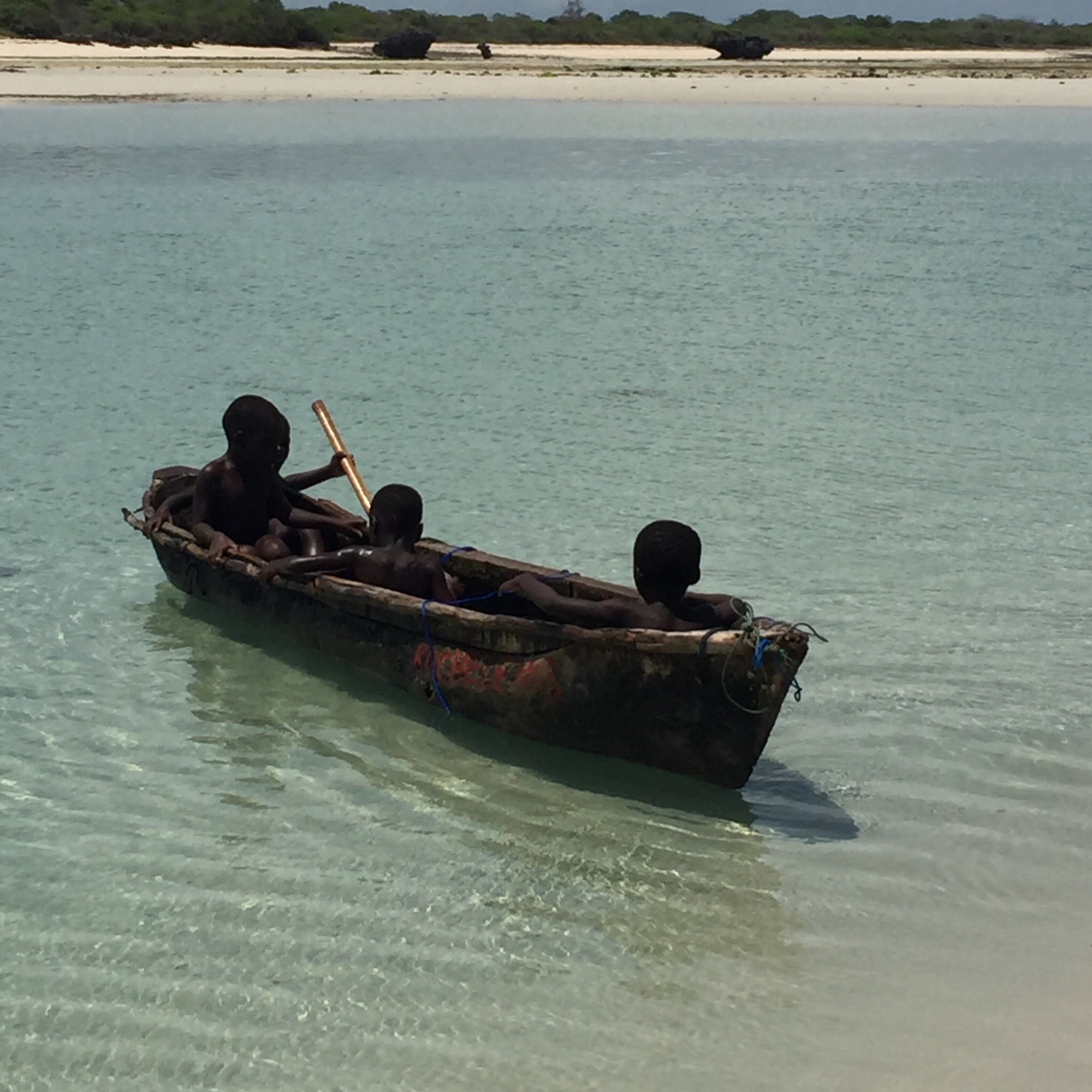 four children sitting in a small row boat in a clear, shallow sea