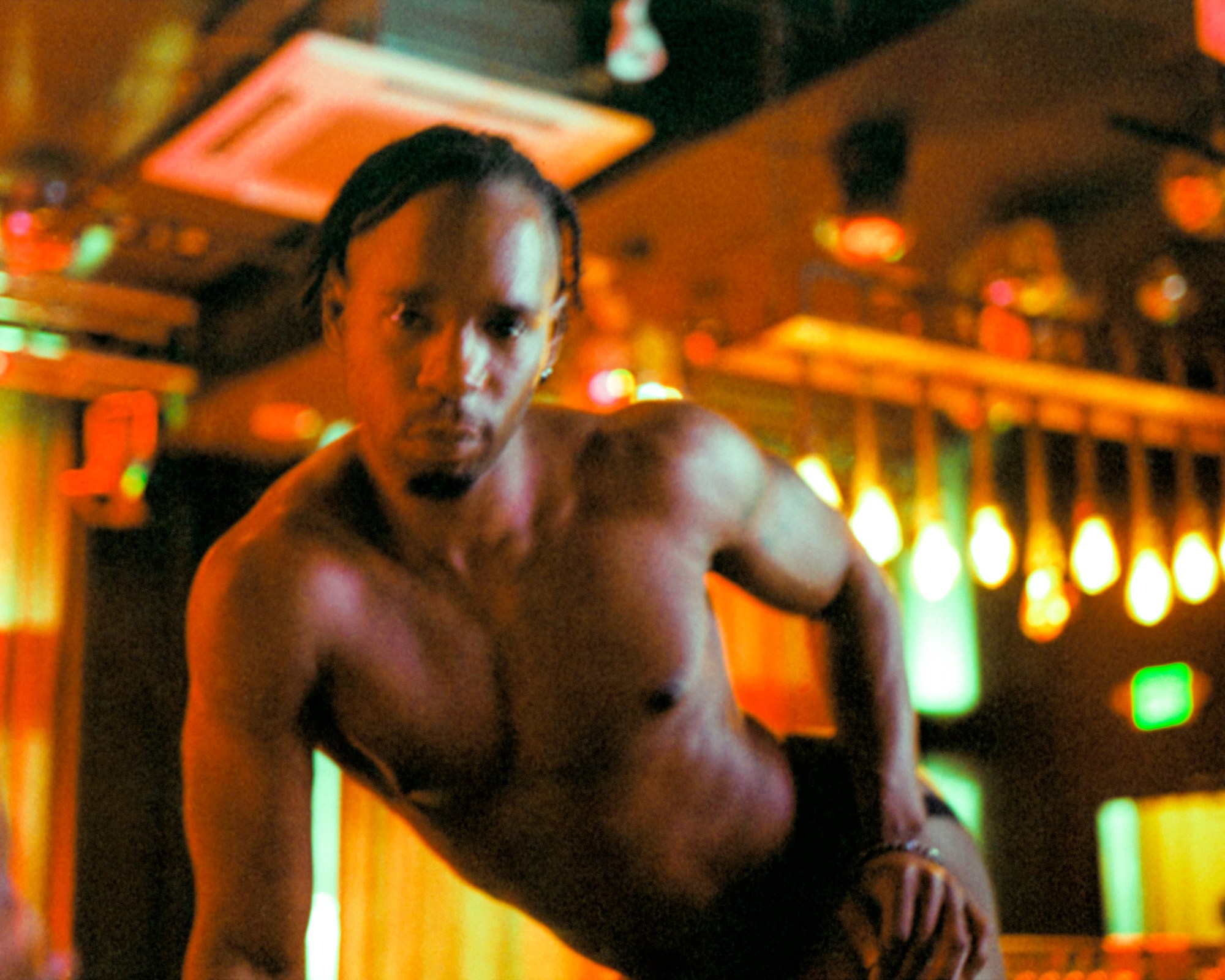 a blurred photograph of a male-presenting person posing topless in an empty nightclub