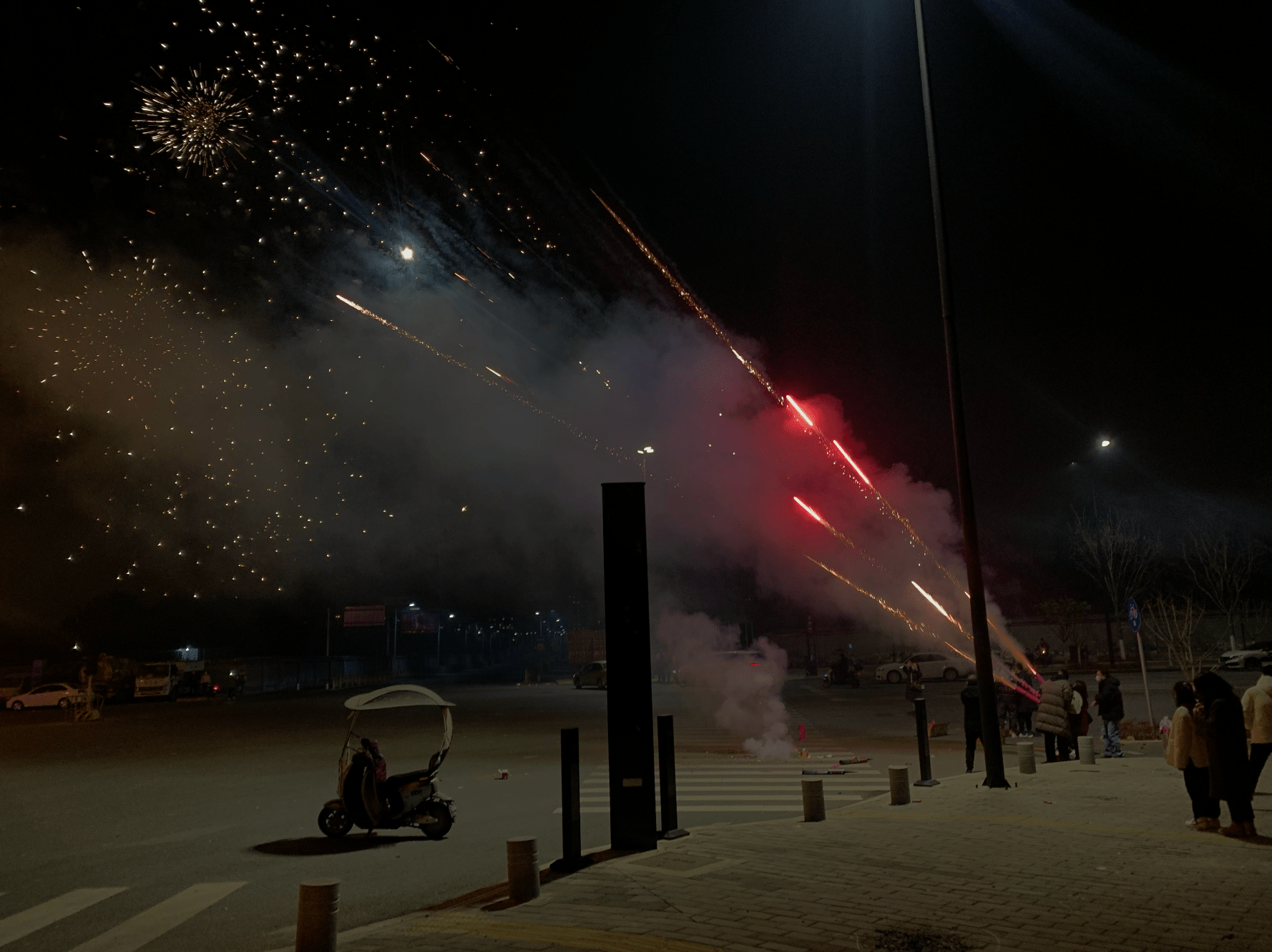 a dark street scene with red fireworks captured shooting into the sky