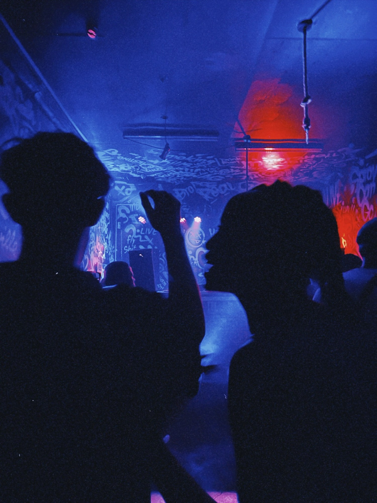 silhouettes of friends in a UV-lit club venue with graffiti on the walls