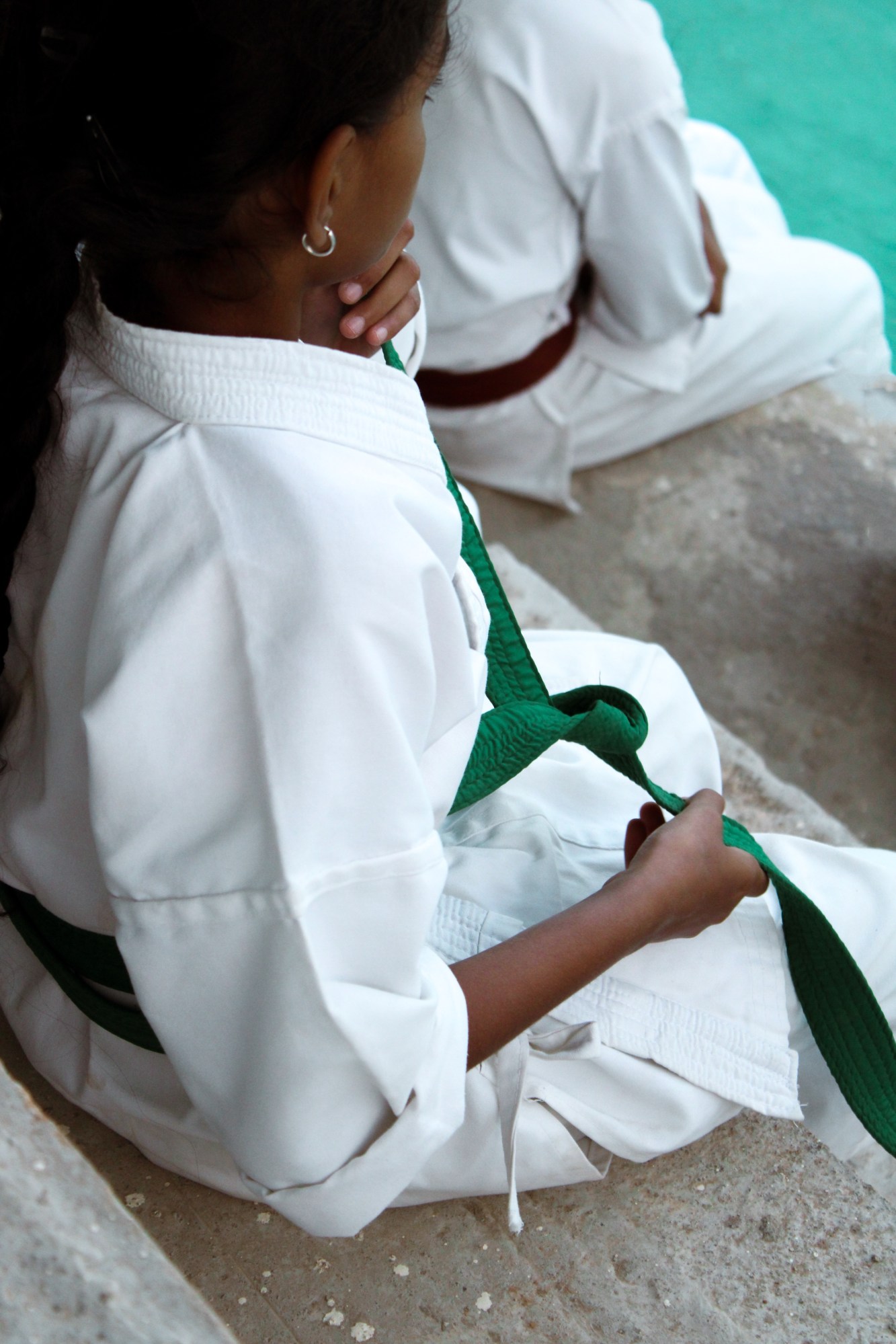 an over the shoulder shot of a young girl tying up her green karate belt