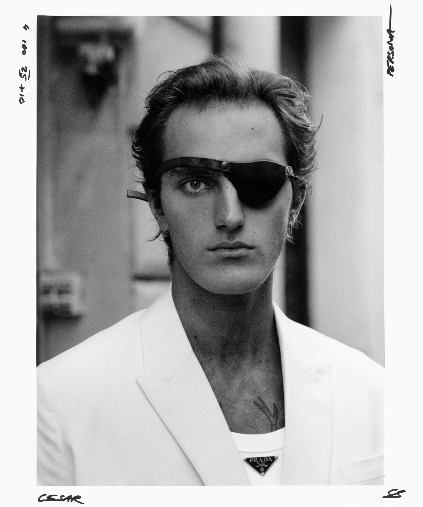 black-and-white image of a person in a white blazer, prada tank top and eye patch