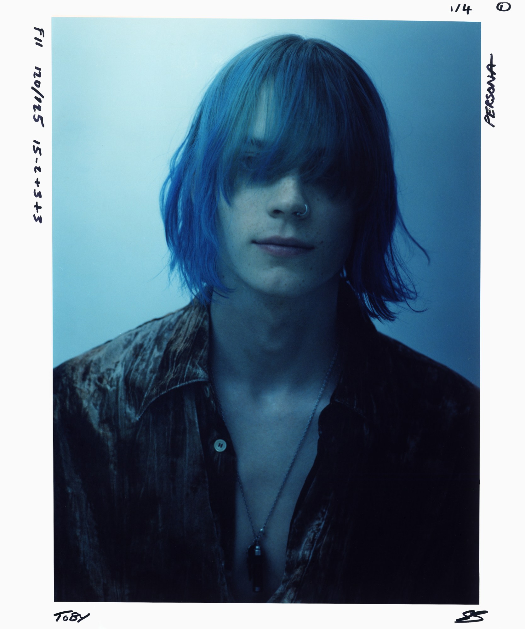 blue toned image of a person with blue hair and open shirt with pendant necklace