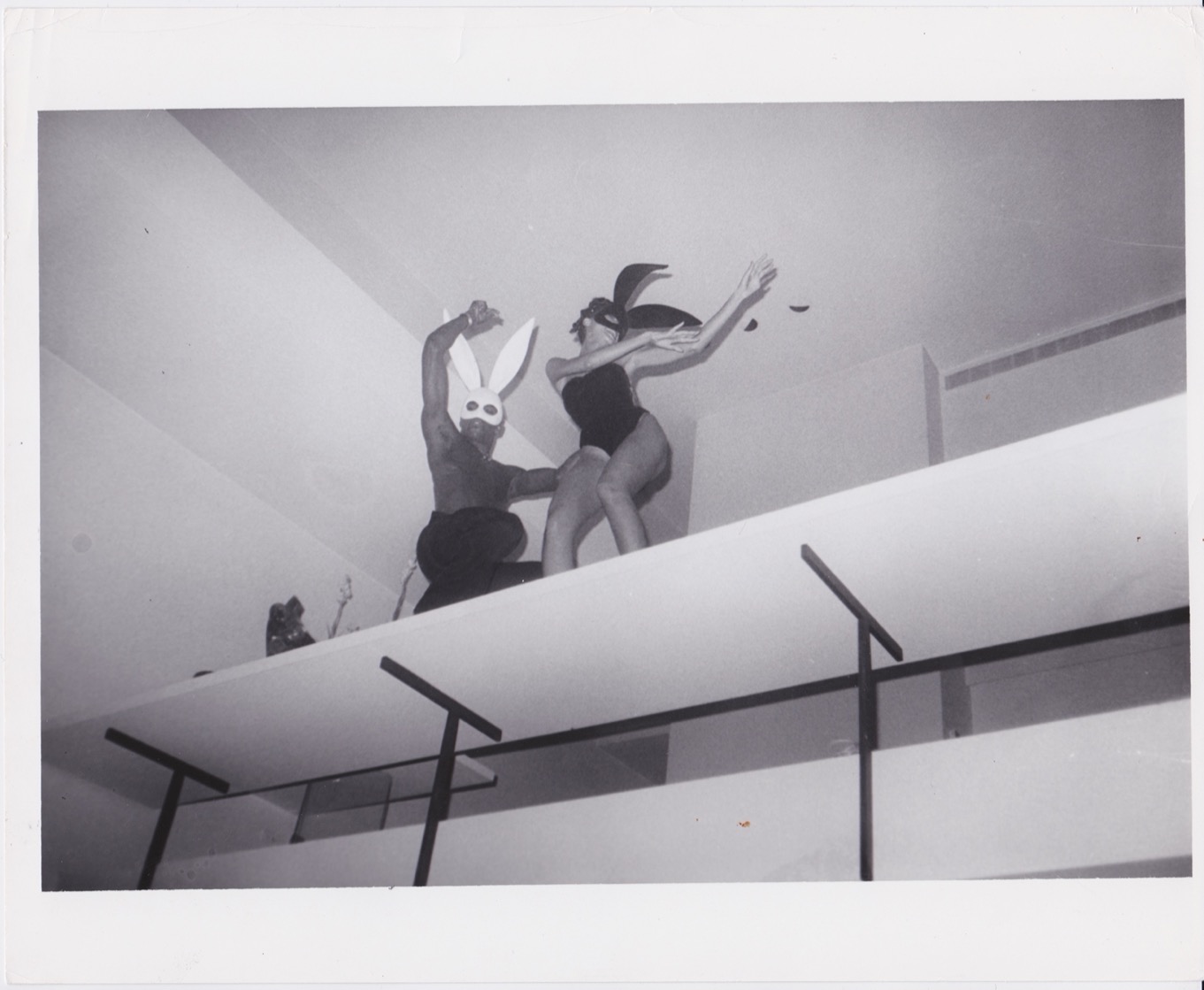 two semi-clothed dancers wearing rabbit masks perform on an overhead podium