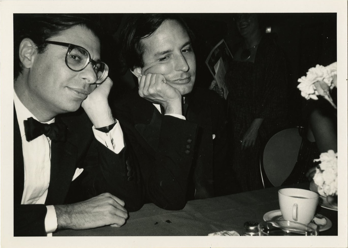 two men in suits sit at a table, heads resting on their hands