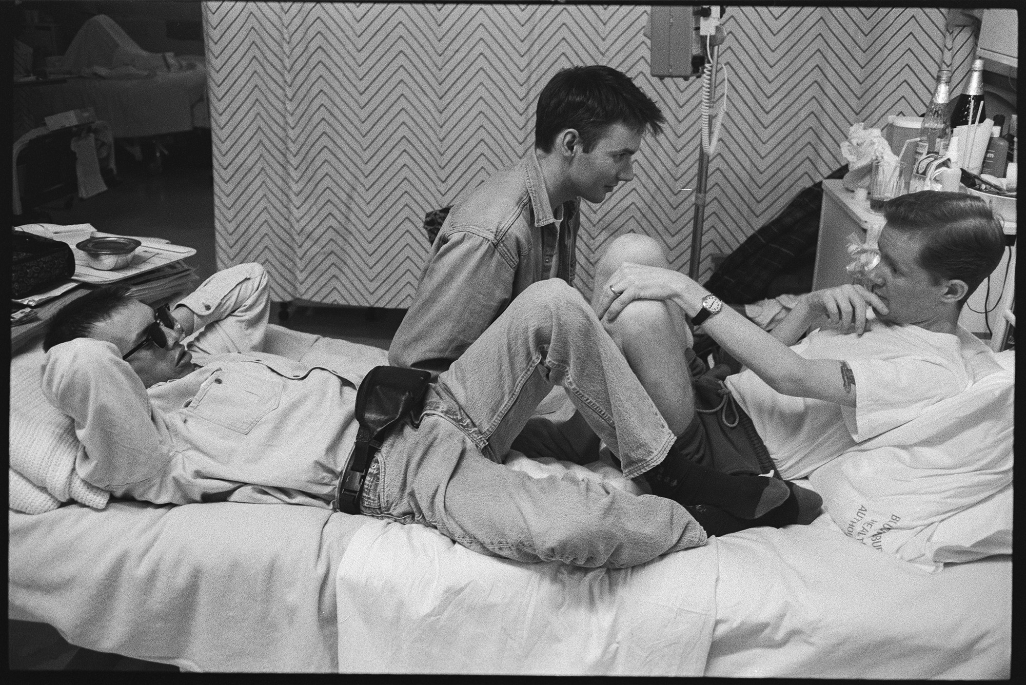 Exclusive photograph from Gideon Mendel's exhibition 'The Ward Revisited' at The Fitzrovia Chapel of three gay men chatting while sitting in a hospital bed in Broderip AIDS ward in Middlesex Hospital.