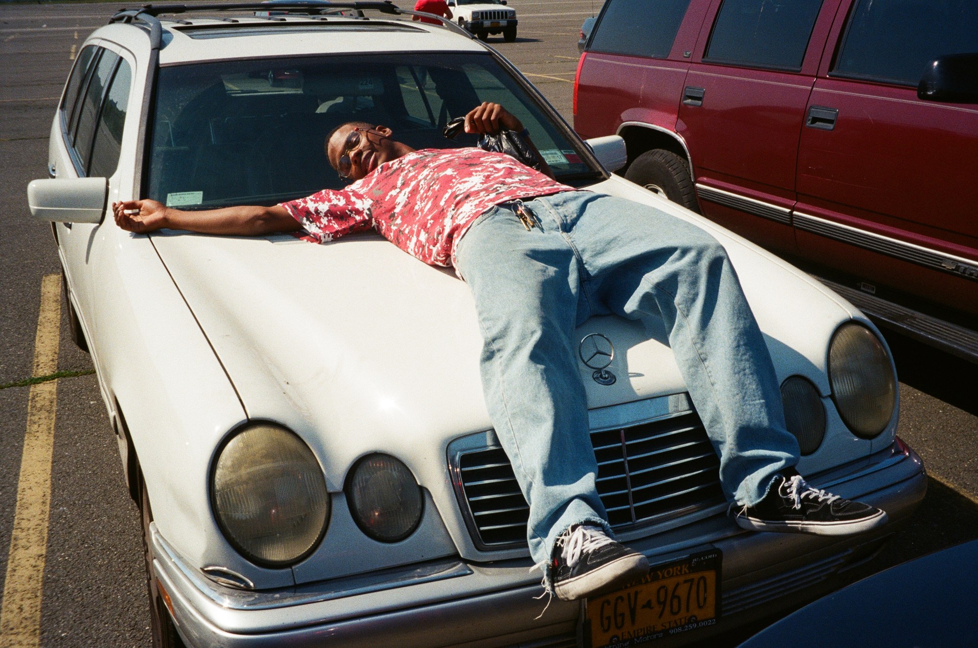 a man lying on top of an old white mercedes car in jeans and vans