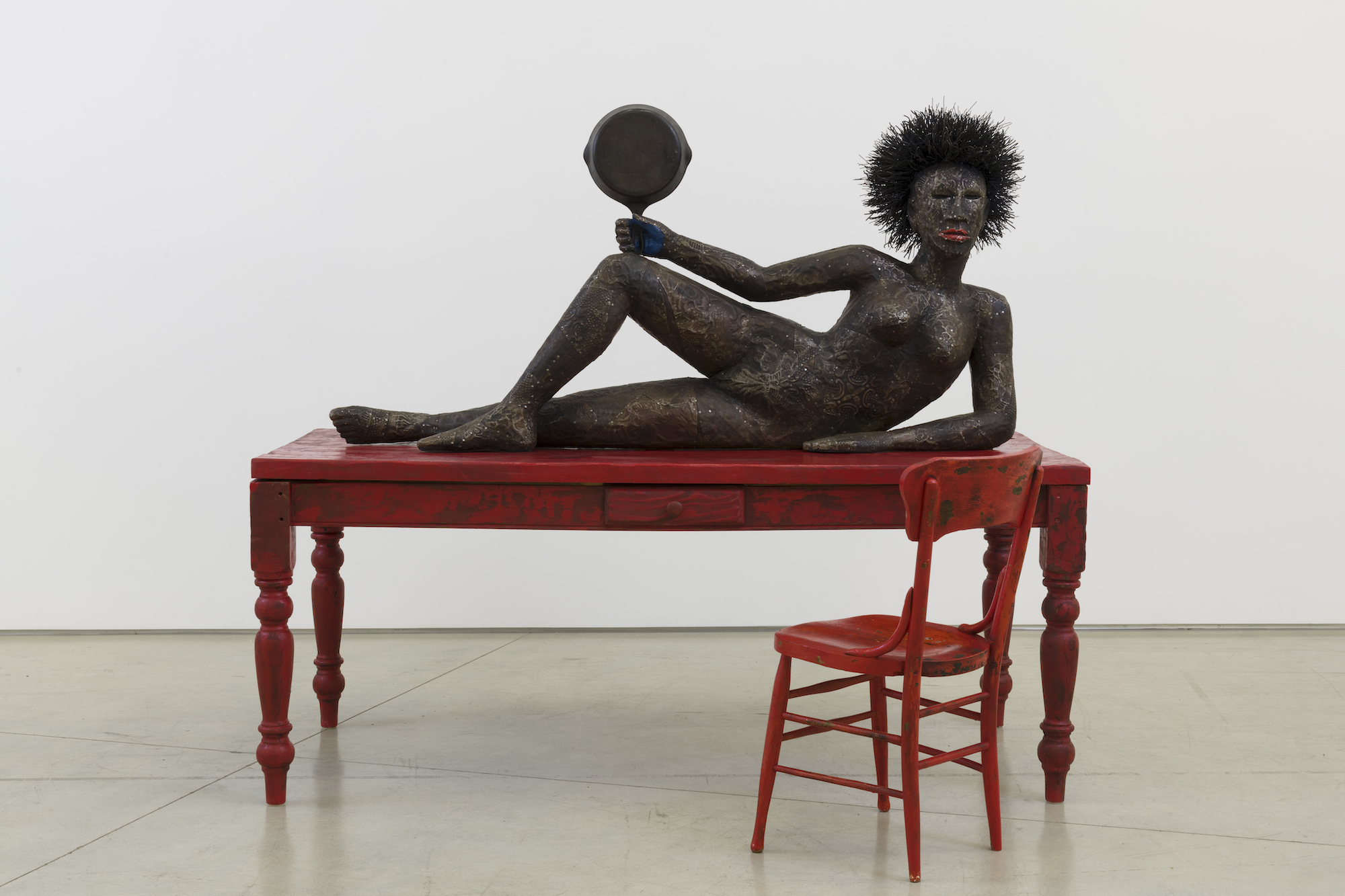 A sculpture of a woman lying on a red table next to a red chair