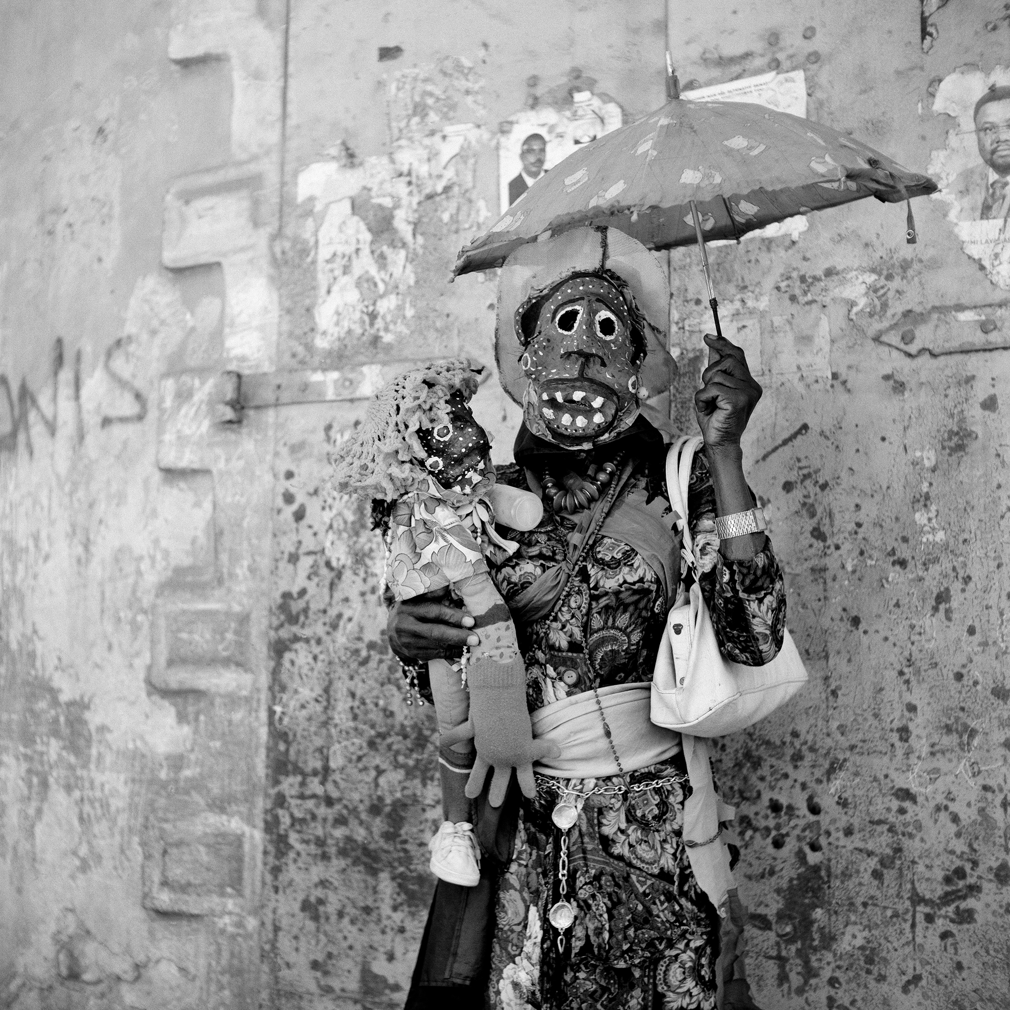 A woman wearing a traditional Haitian mask, carrying a doll and umbrella.