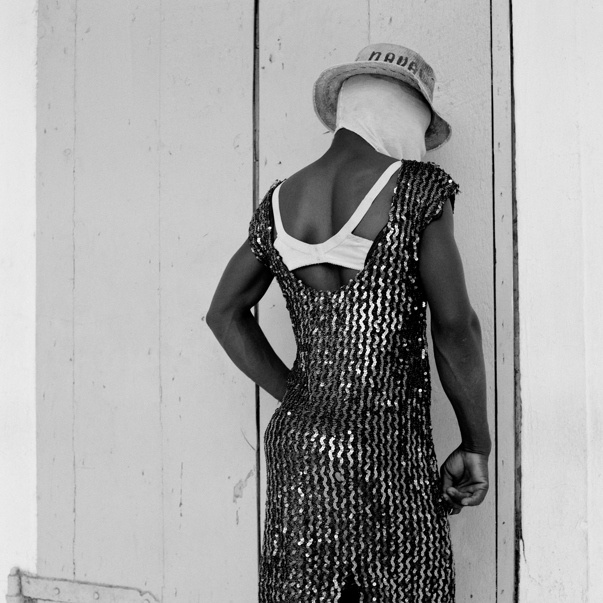 A festival goer wearing a sequined dress and straw hat turning toward a wall.