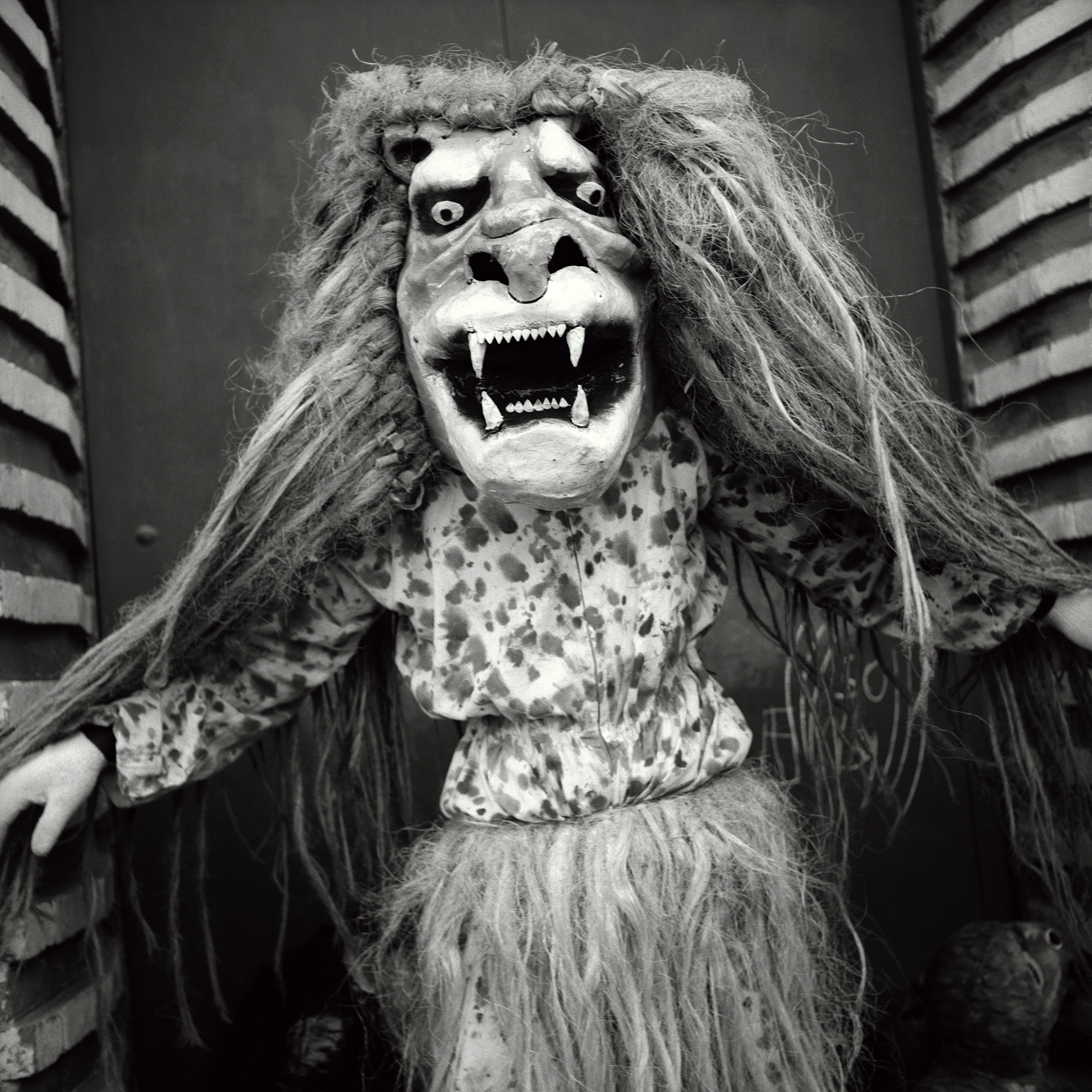 A festival goer wearing a large lion mask and splatter print jacket.