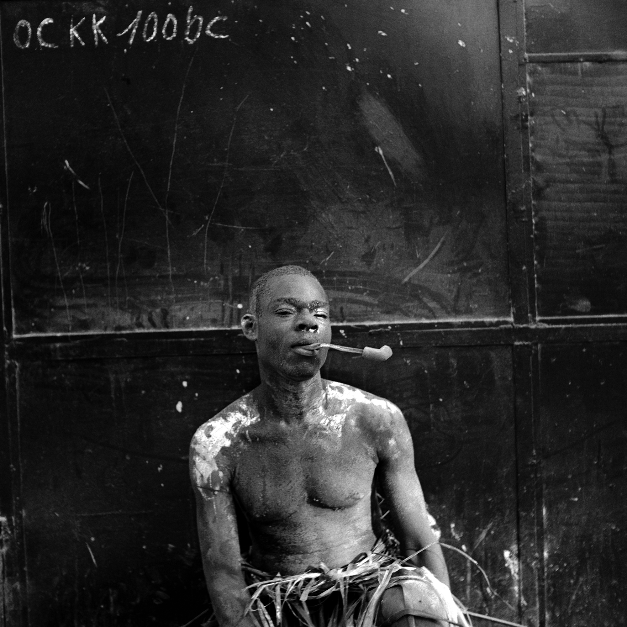 A young man posing for a portrait at Haitian Kanaval holding a pipe in his mouth.