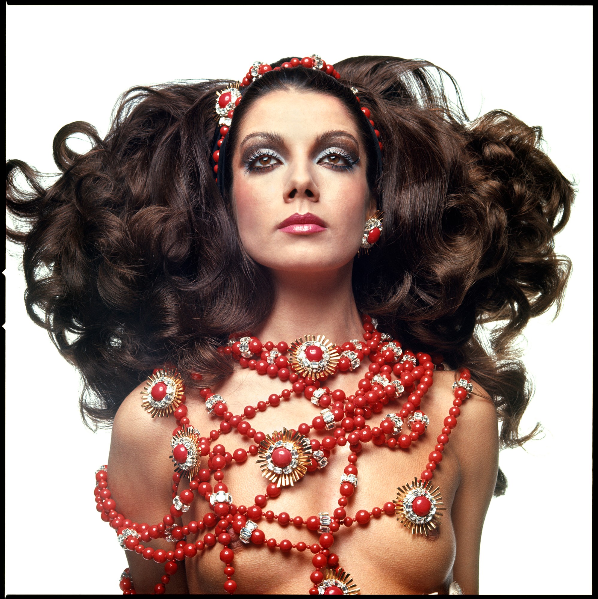 1960s model with brown hair wearing red beads over naked chest