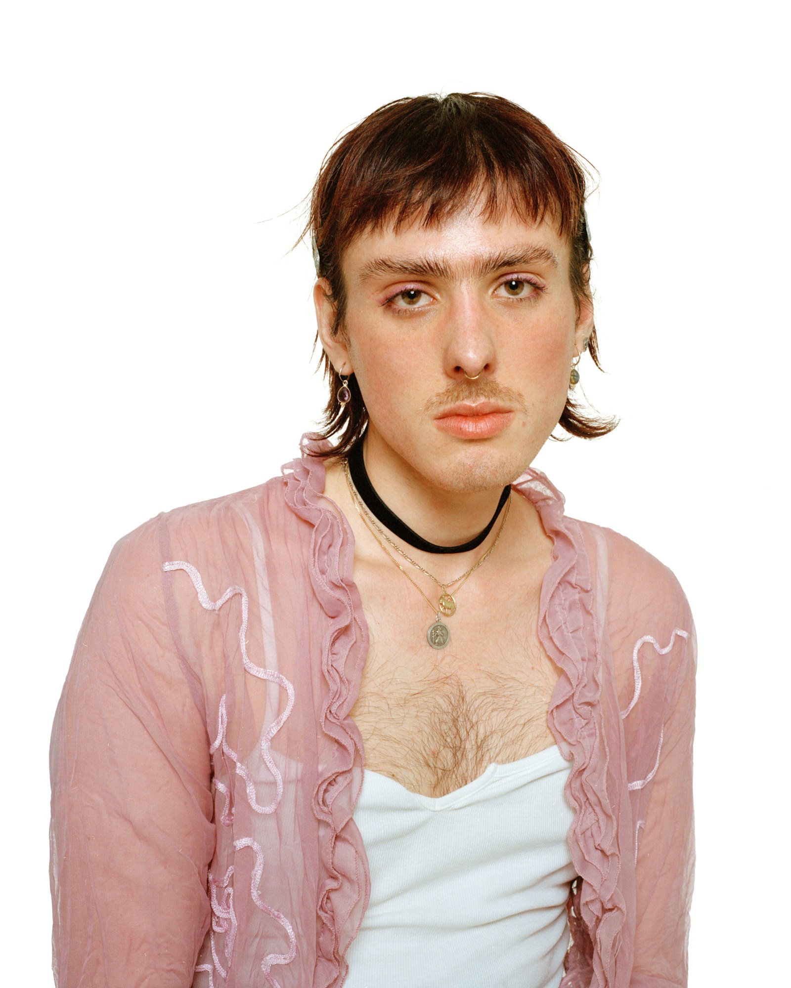 a young person with a hairy chest wears a vest top and pink chemise, their eyebrows are well groomed