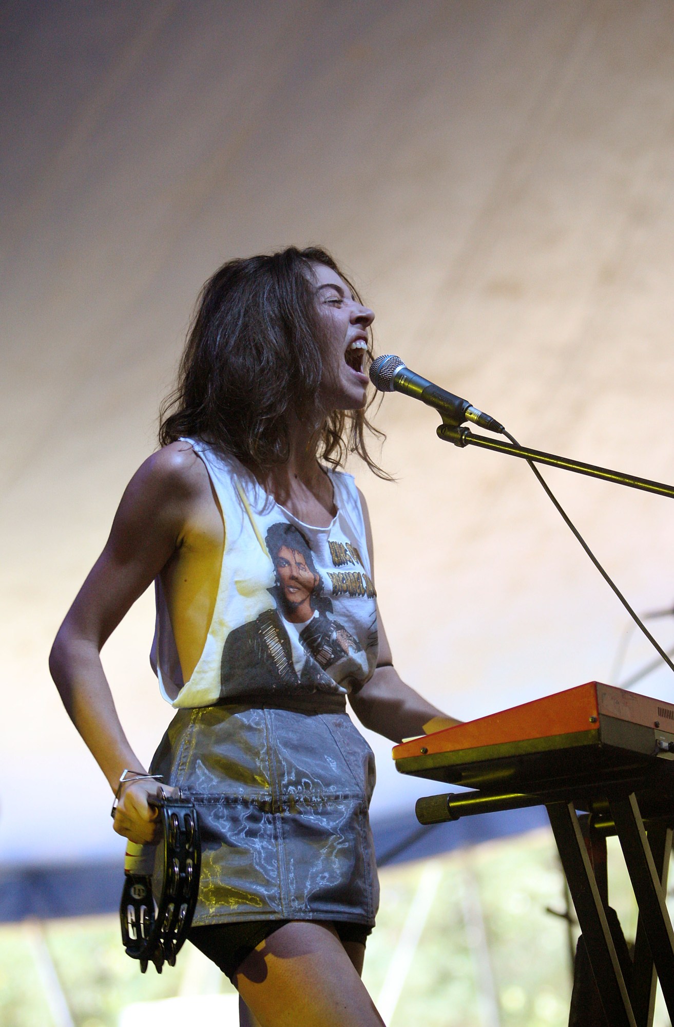 caroline polachek performing in a cut-up michael jackson tee and shimmery mini skirt. she holds a tambourine