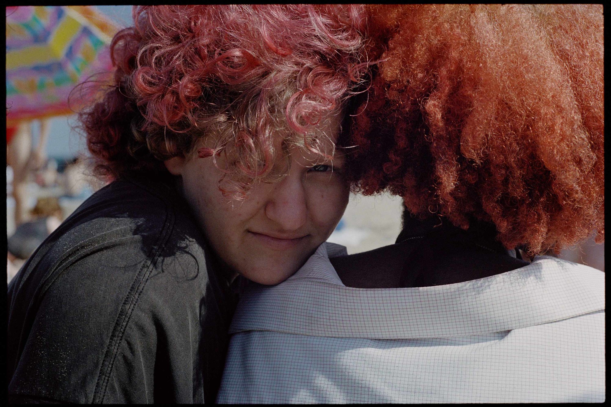 two teenagers with curly red hair stood next to each other. one faces away from the camera. the other is rested on their shoulder, looking into the lens.